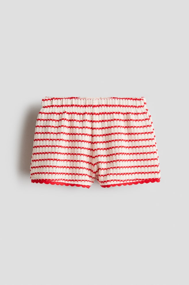 The shorts are being presented from the front, displaying a soft, textured knit with alternating red and cream horizontal stripes. An elasticated waist is gathering the top of the shorts, and the leg openings are featuring red scalloped hems. - 1