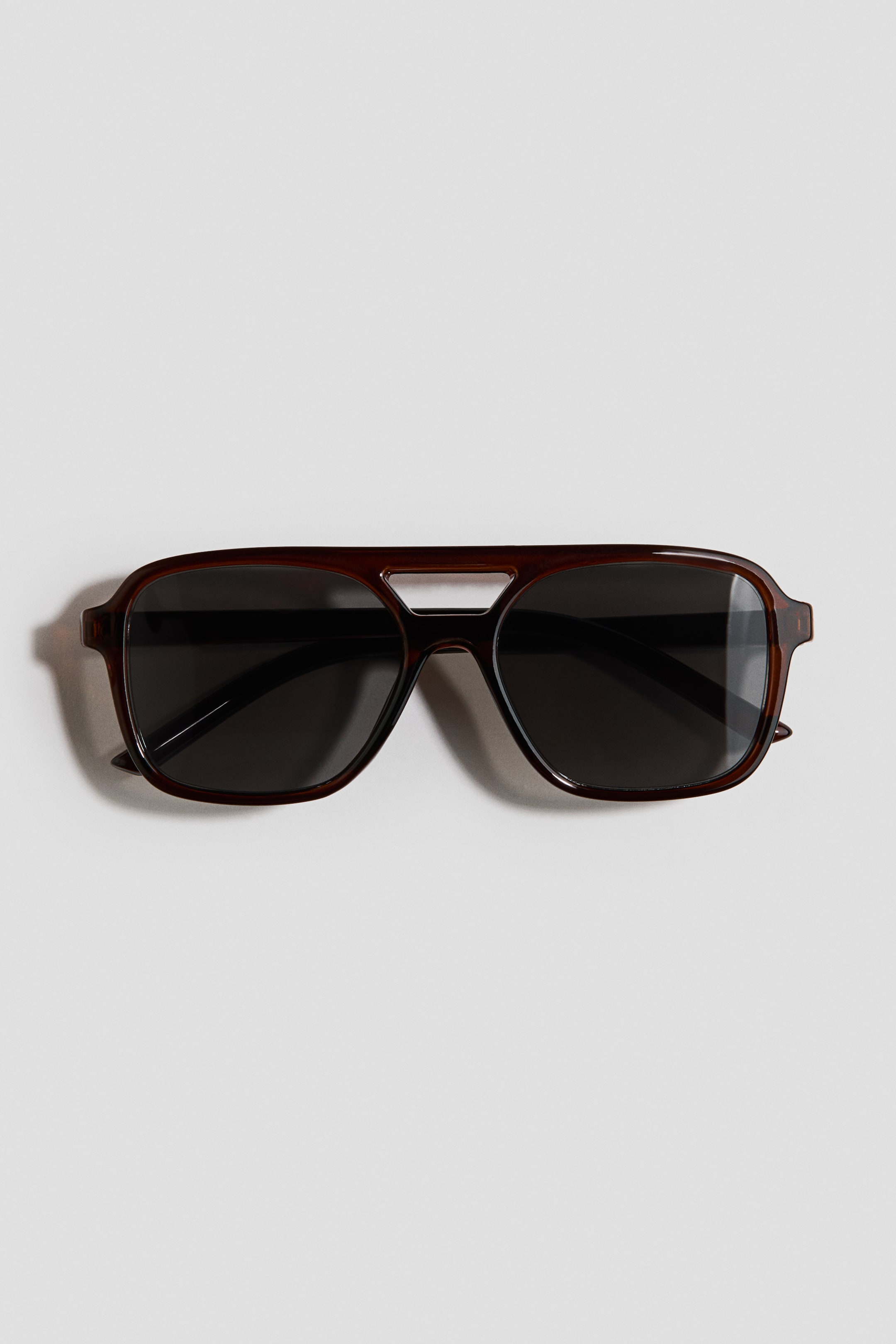 Voir une image plus grande: DEVANT : Les lunettes de soleil présentent des montures en plastique brun foncé avec un design à double pont et des branches visibles. Les verres rectangulaires teintés foncés sont intégrés dans les montures.