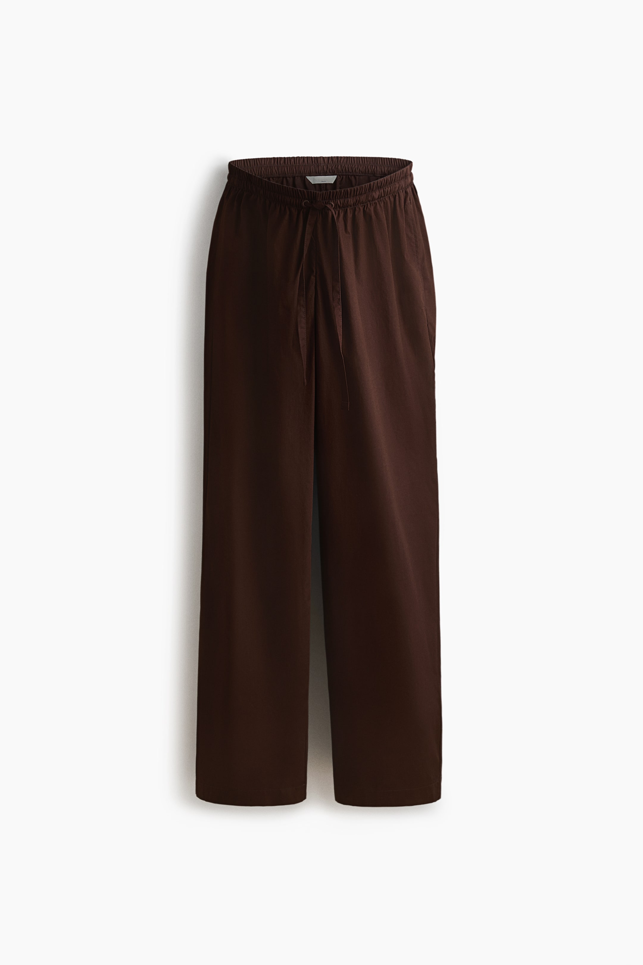 Größeres Bild ansehen: Braune Hosen hängen flach und sind von vorne präsentiert, mit einem weiten, geraden Schnitt. Der elastische, geraffte Bund zeigt vorne mittig eine Kordelzugbindung, und dezente Seitentaschen erscheinen an den Hüften.