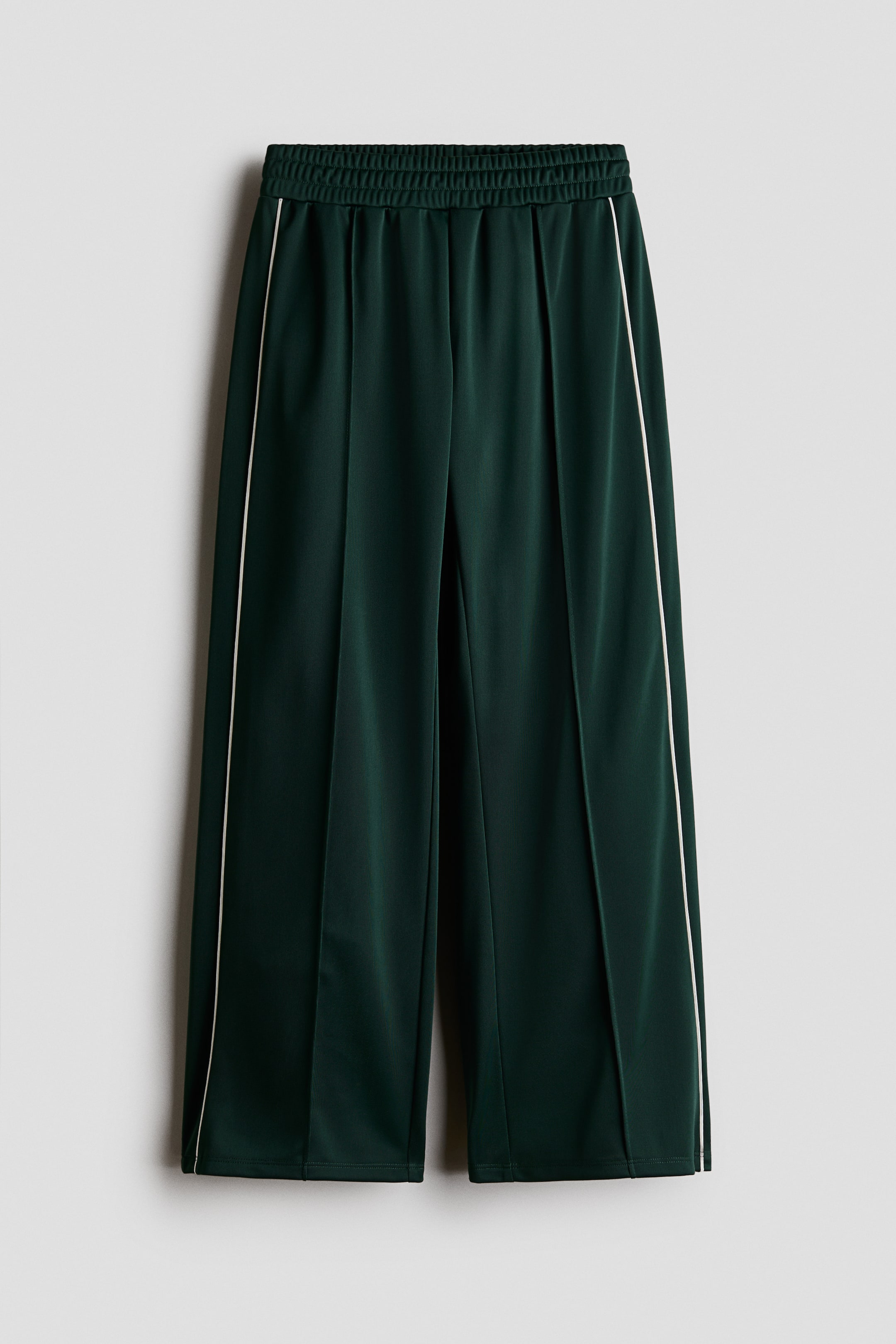 View larger image: Dark green wide-leg pants featuring an elasticated waistband, vertical pressed creases down the front of each leg, and white stripes detailing each side seam.