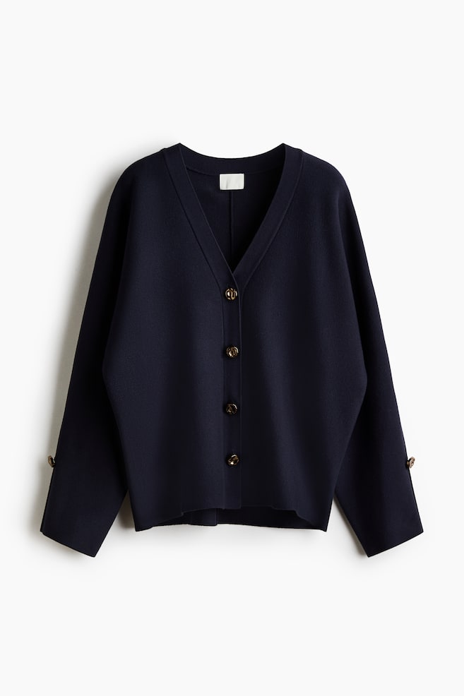 A navy blue V-neck cardigan is shown from the front, showcasing a relaxed fit, a four-button front fastening with tortoiseshell-style buttons, and long sleeves with matching decorative buttons near the cuffs. - 1