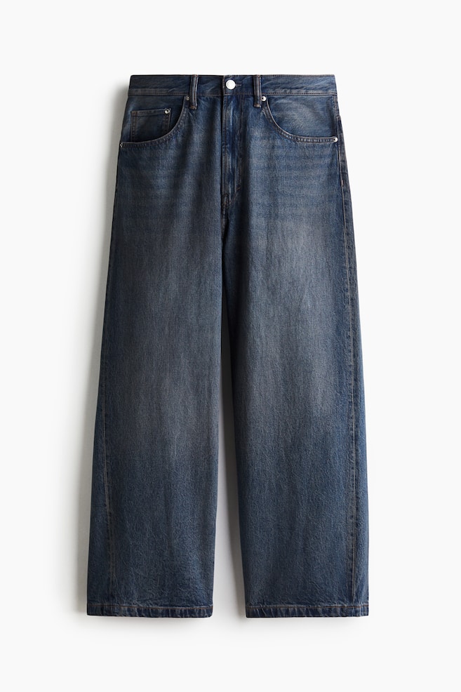 Front view of dark blue, rigid cotton denim 5-pocket jeans, featuring subtle fading on the thighs, a regular waist, and a zip fly. These jeans are presenting a baggy fit with a rounded leg, a dropped crotch, and plenty of room throughout, appearing stacked at the ankle. - 1