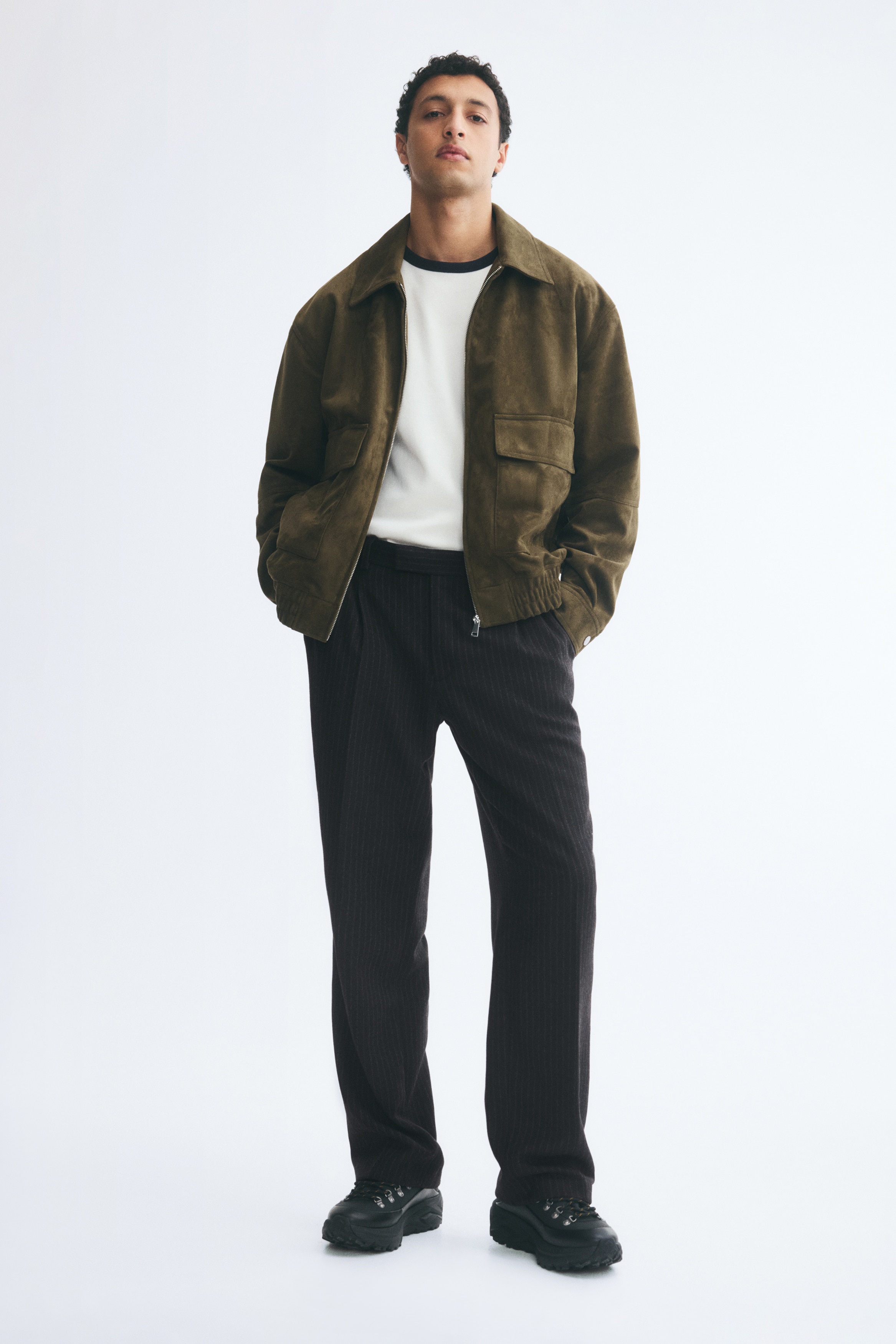 A pair of dark grey pinstripe trousers is hanging front-facing, showcasing a straight-leg silhouette with sharp creases running down the centre of each leg. The trousers feature a structured waistband with belt loops and a clean, concealed front fastening.