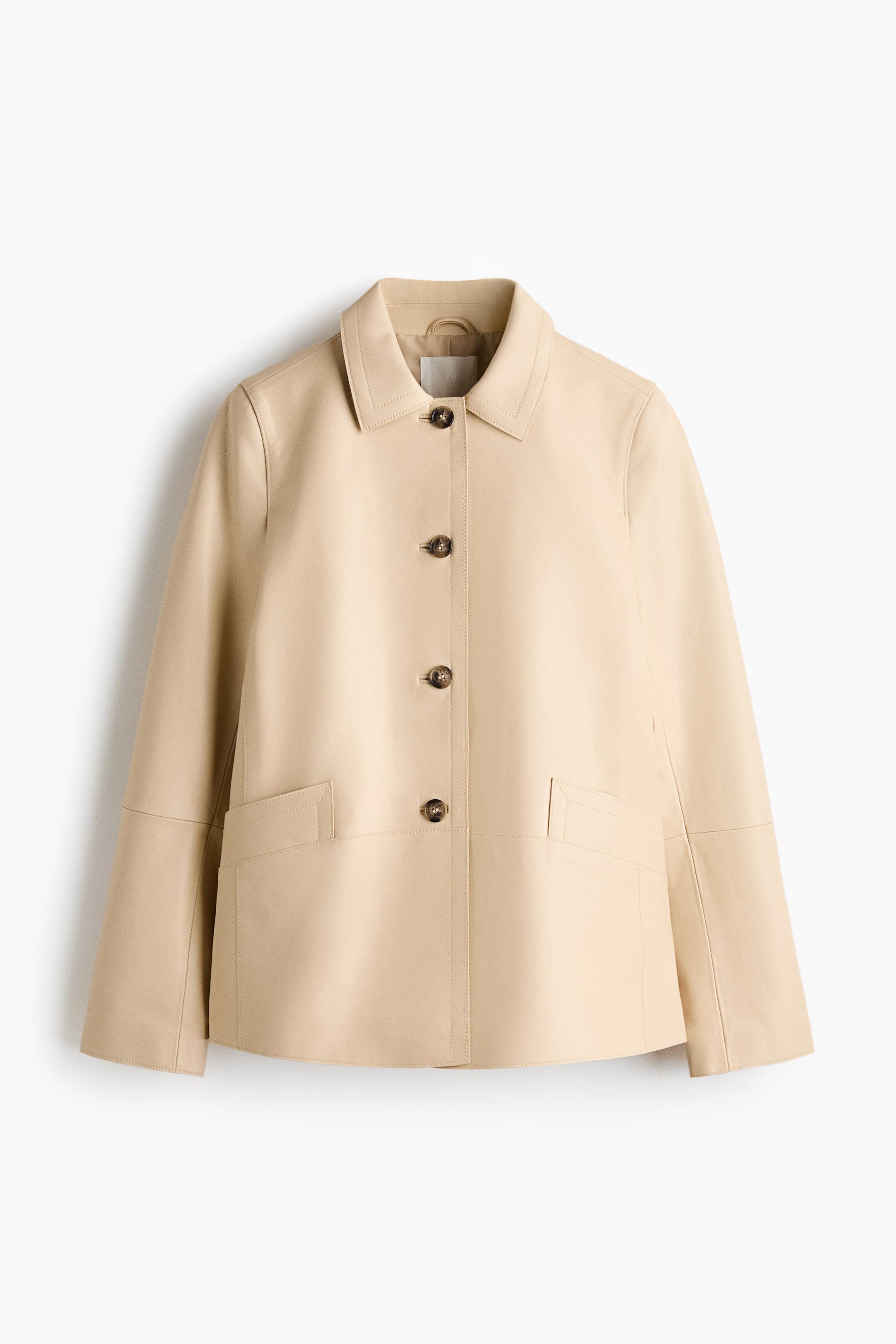 Ampliar la imagen: Una chaqueta de cuero beige claro se presenta de frente, con un cuello en punta y cuatro botones visibles en el frente. Está diseñada con dos bolsillos de ojal frontales y puños que incluyen una abertura y cierre de botón.