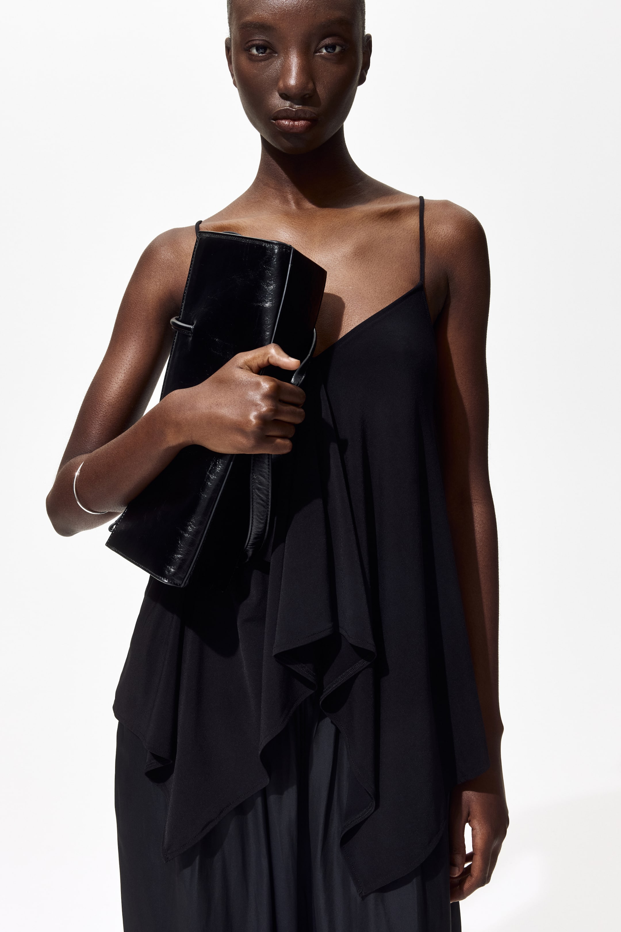 Größeres Bild ansehen: Eine rechteckige schwarze Clutch-Tasche mit einer Lederstruktur im Used-Look wird von einer Hand frontal gehalten, die ein Riemendetail an der Seite zeigt.