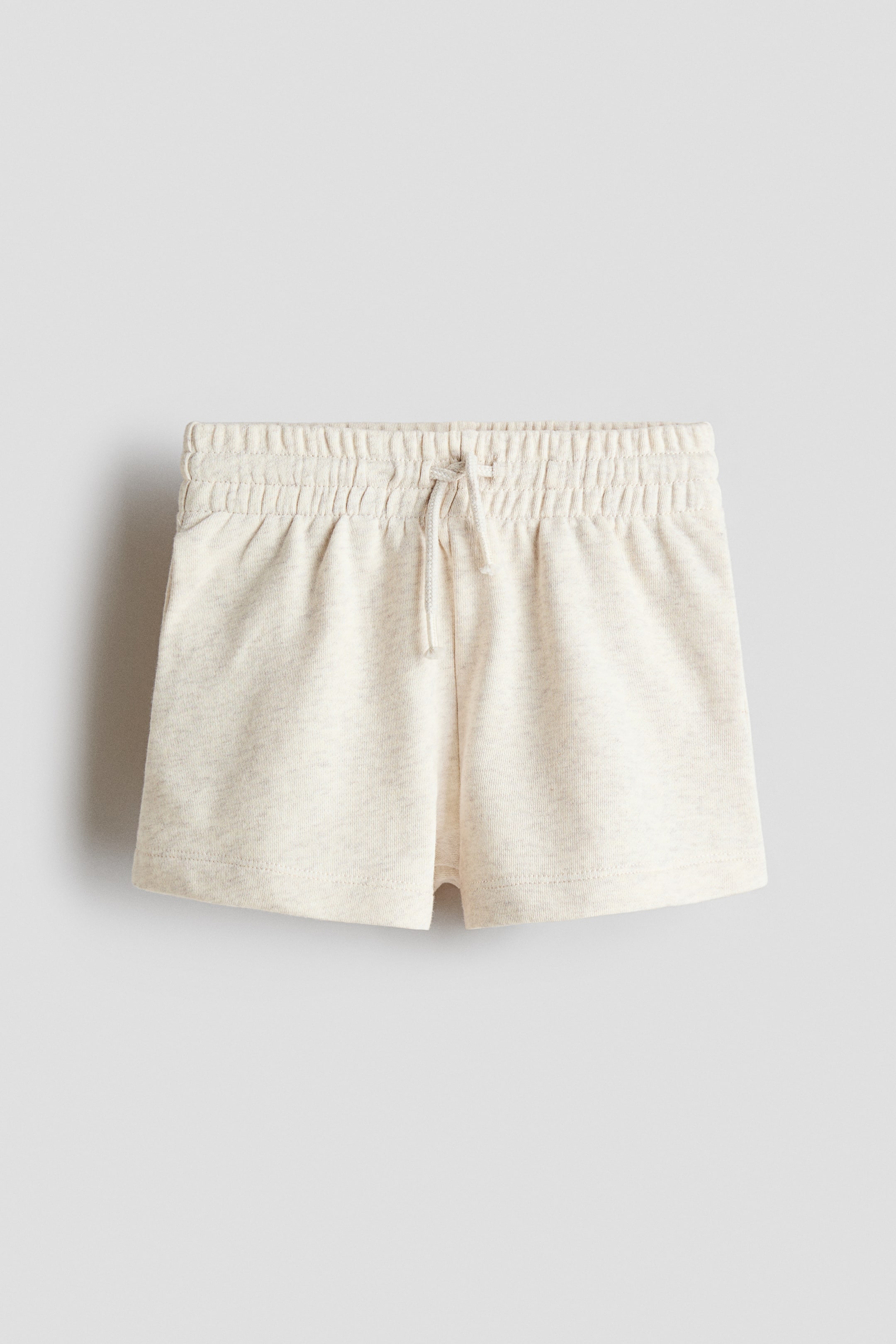 View larger image: Shorts in a light beige marled sweatshirt fabric are showing their front view, featuring an elasticated, gathered waist with a visible drawstring tied at the center and discreet side seam pockets.