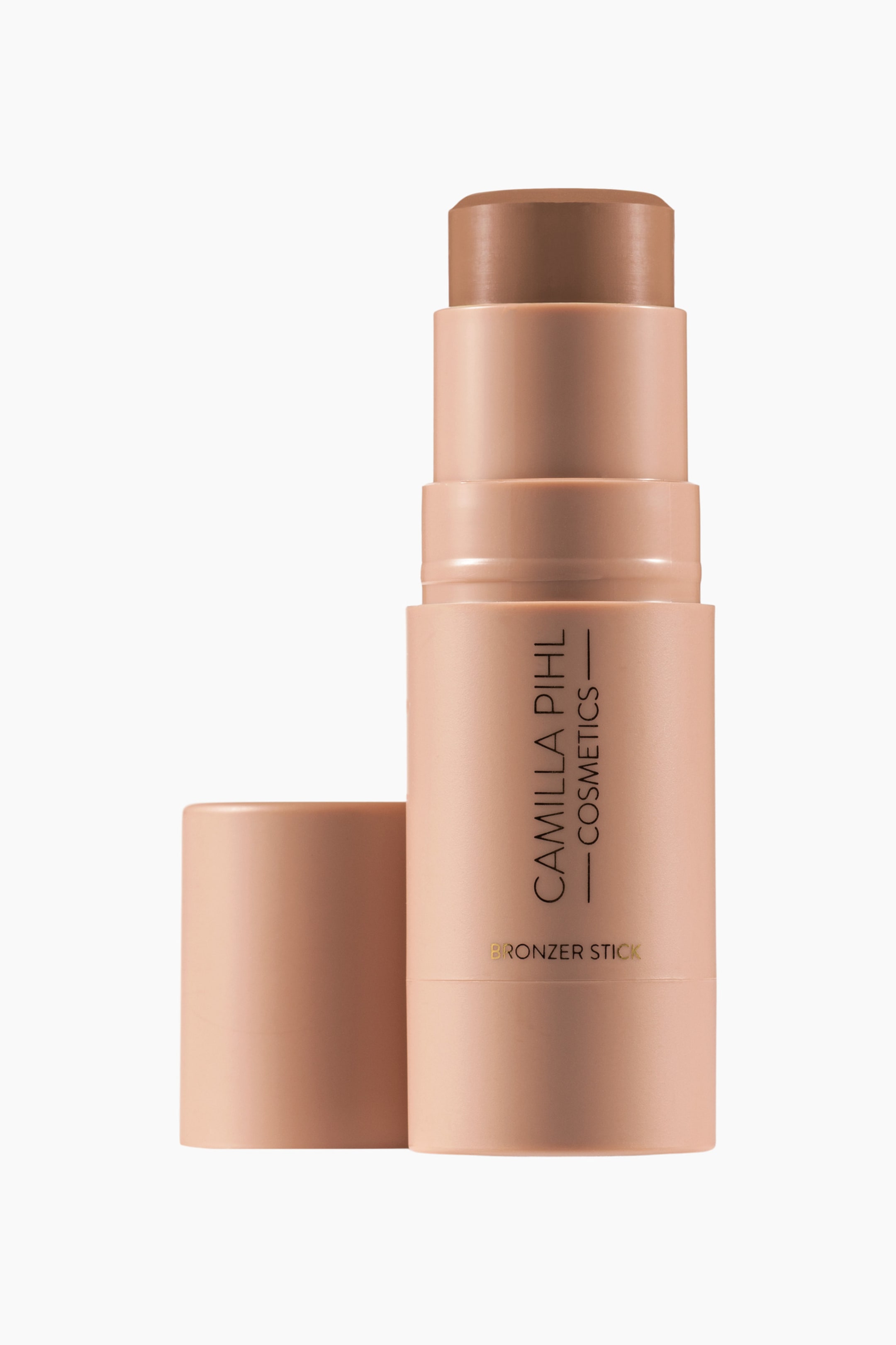 Visa större bild: En bronzerstick står upprätt, med ett matt persikofärgat cylindriskt hölje med "Camilla Pihl Cosmetics Bronzer Stick" tryckt på sidan, och den bruna bronzerprodukten som sträcker sig från dess rundade topp. Dess matchande cylindriska lock ligger på sidan bredvid sticken.