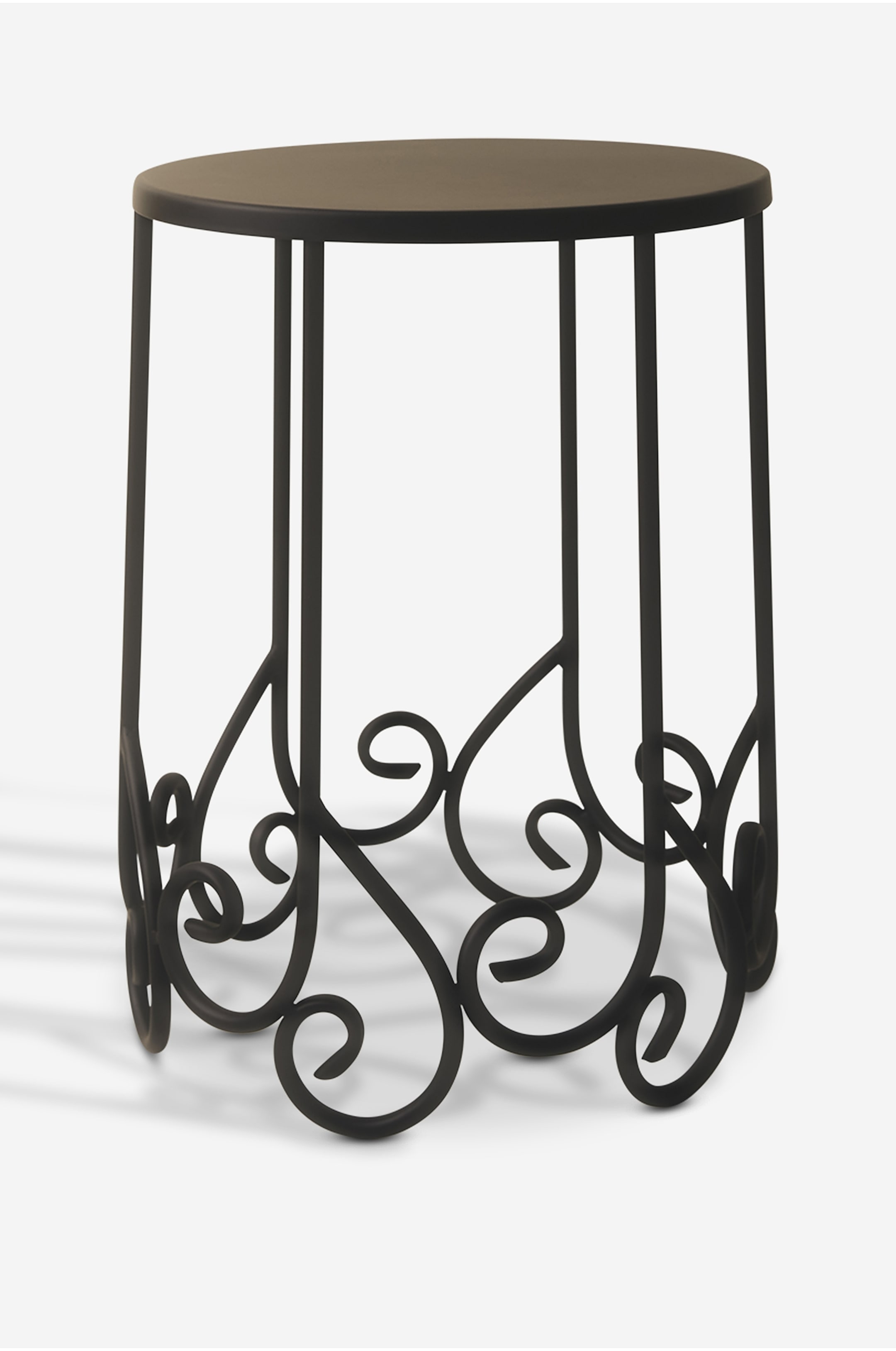 Visa större bild: Ett svart metallsidobord visar en plan, cirkulär bordsskiva som bärs upp av smala, lodräta ben. Benen sträcker sig nedåt och övergår i en intrikat design av snirkliga, dekorativa ornament som bildar underredet.