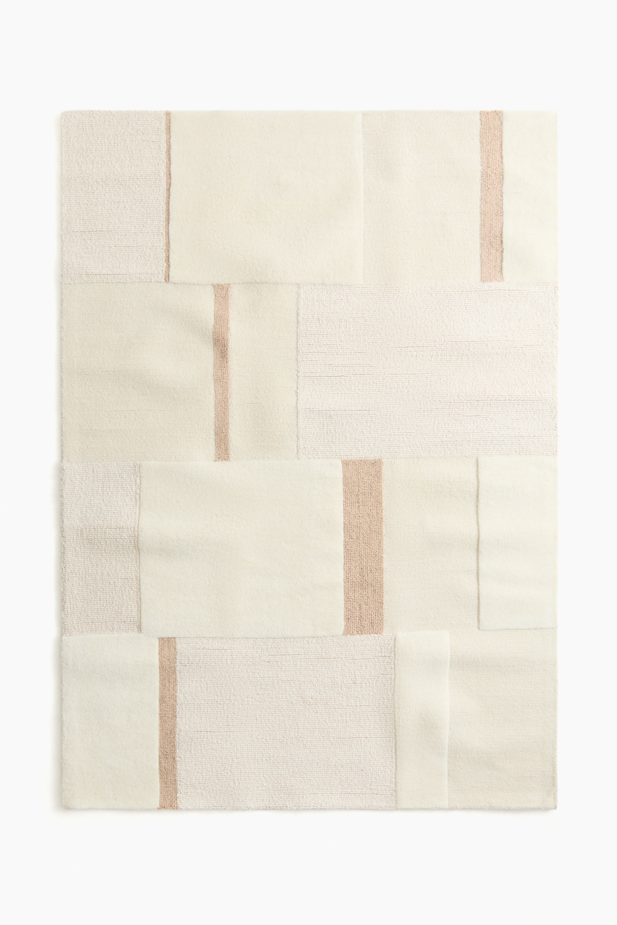 Nagyobb kép megtekintése: A krémszínű szőnyeg geometrikus foltvarrás dizájnt mutat be, amely sima téglalap alakú paneleket kombinál texturált, szövött panelekkel. Vékony, világosbarna függőleges csíkok vannak beépítve a dizájnba, amelyek tovább növelik a texturális kontrasztot.