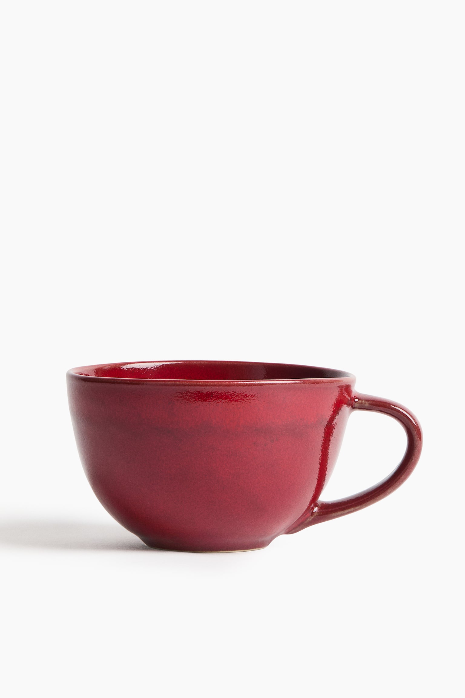 A stoneware tea mug, shown facing the front, features a wide, rounded bowl-style body and a curved loop handle on the right. The mug has a glossy, deep red reactive glaze with subtle tonal variations across its surface. - 1