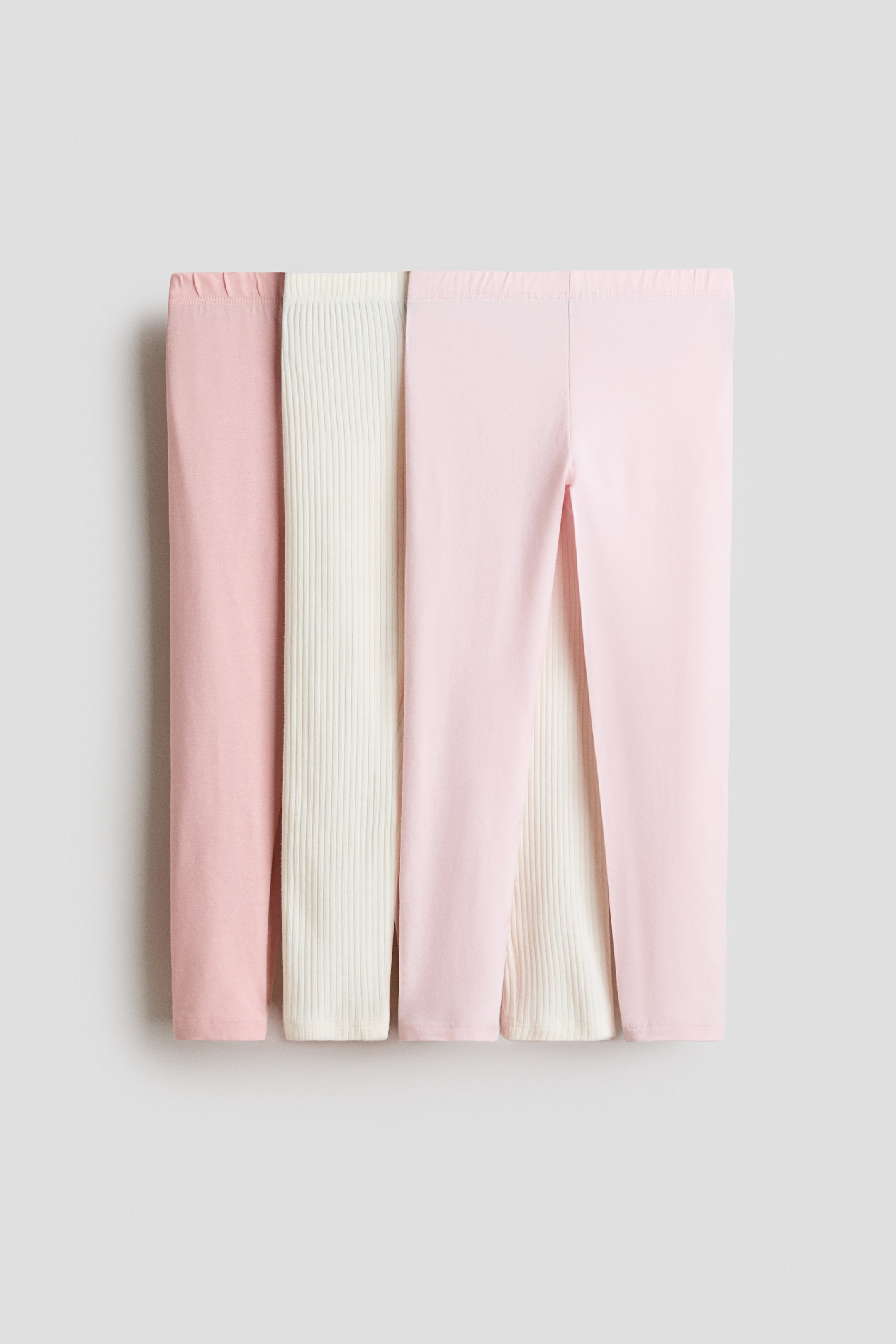 View larger image: Leggings are presented in a horizontal stack, showing two solid pink pairs and two ribbed cream pairs, each featuring an elasticated waist.