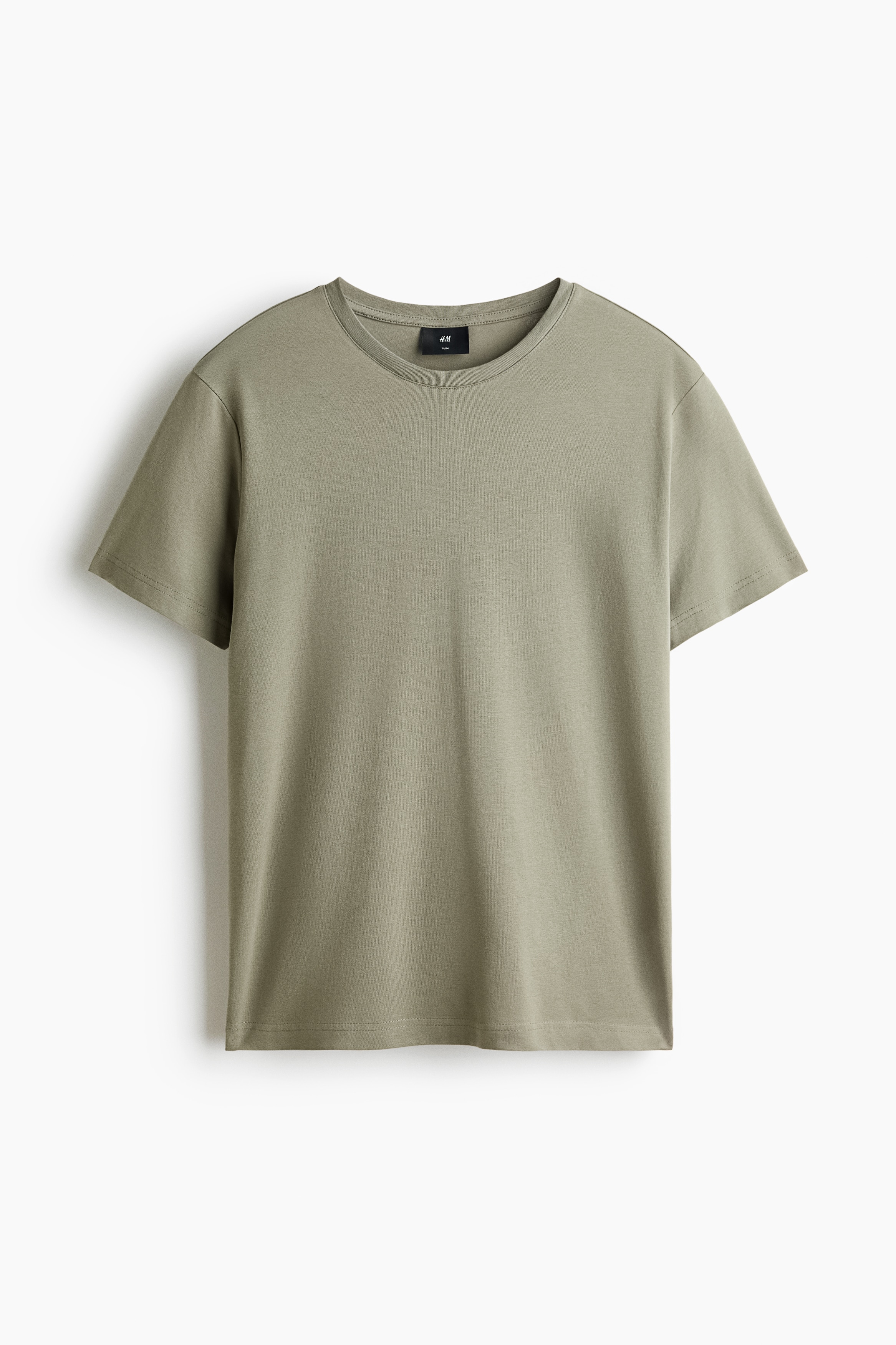 A light sage green, slim-fit t-shirt in lightweight cotton jersey is being worn by the model, tucked into light-wash blue jeans. The tee features a round, rib-trimmed neckline, short sleeves, and a fitted silhouette.