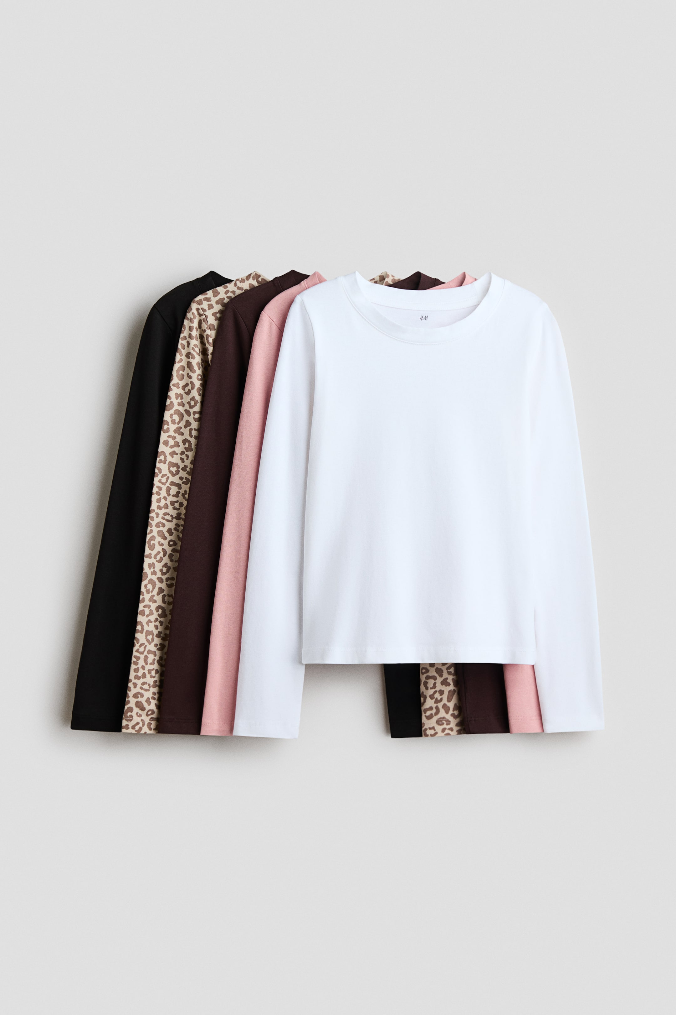 View larger image: Five long-sleeve tops are stacked, with a white crew neck top presenting its front, partially obscuring a pink, a dark brown, a tan leopard print, and a black long-sleeve top.