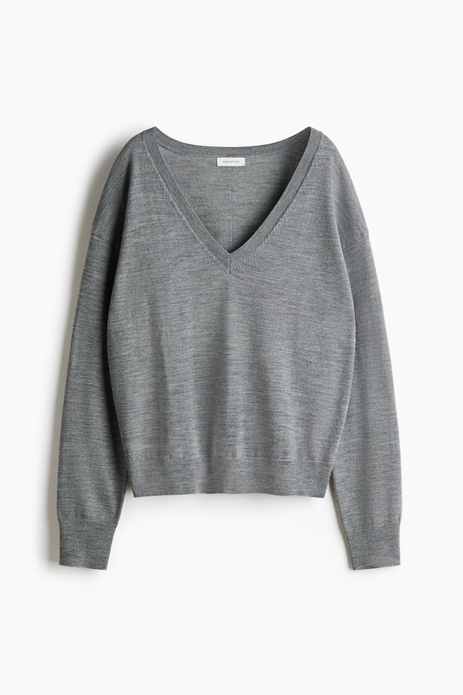 Uma camisola de malha cinzenta Ã© apresentada de frente, com um decote em V profundo com acabamento canelado e ombros descaÃ­dos. A camisola destaca um corte descontraÃ­do, com mangas compridas terminando em punhos canelados e uma bainha canelada a condizer. - 1