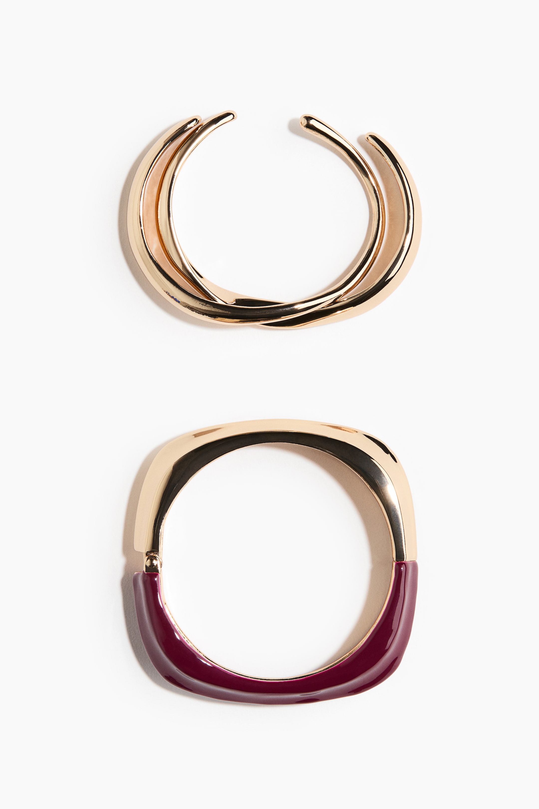 View larger image: A gold-toned open cuff bracelet features two intertwined bands. Below it, a gold-toned hinged bangle presents a rectangular shape with rounded corners and a glossy burgundy section.