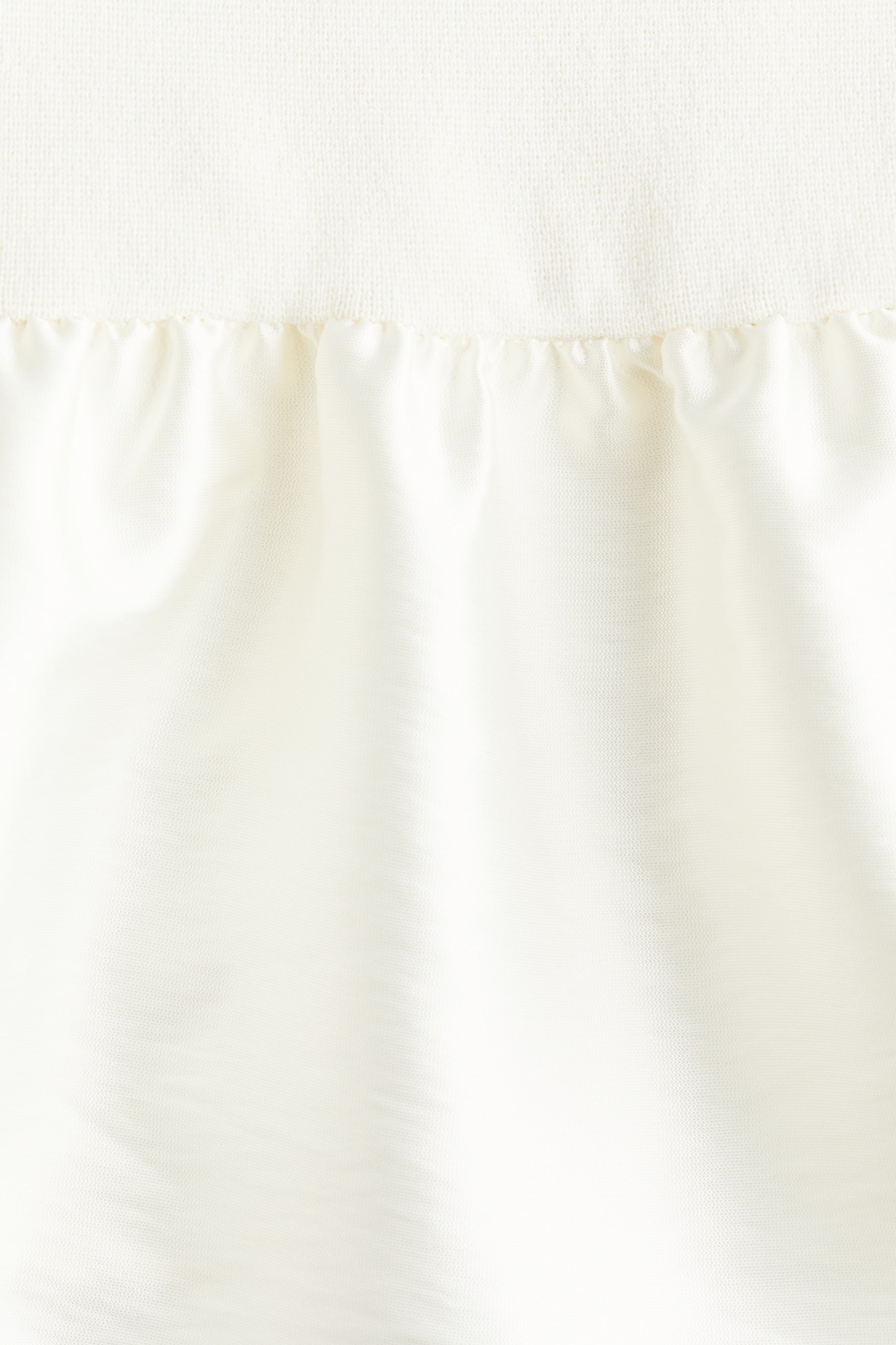 View larger image: A close-up view of a garment shows a textured off-white knit fabric at the top, transitioning to a gathered, smooth off-white fabric below, forming soft folds.