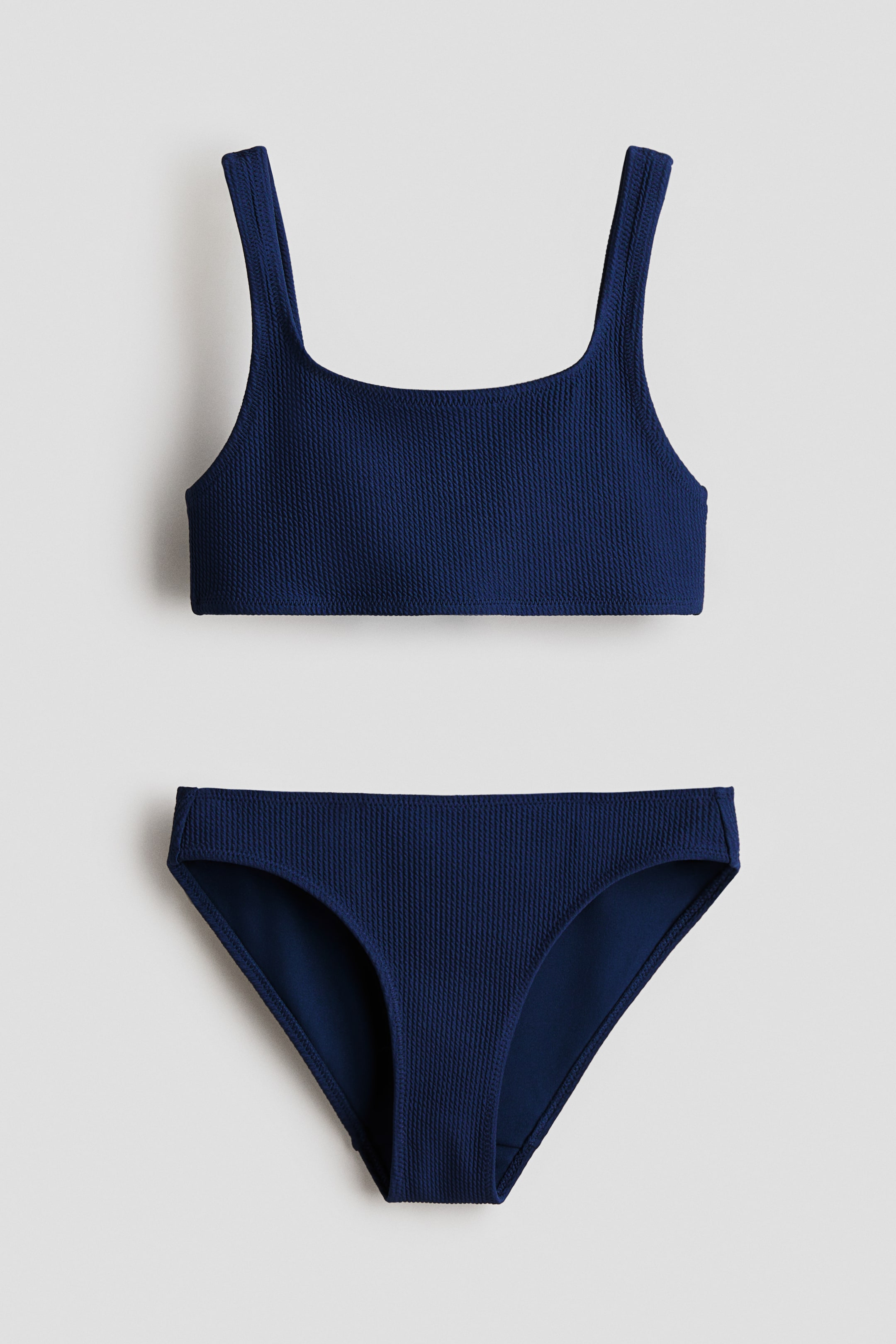 Prikaži veću sliku: Tamnoplavi teksturisani bikini komplet je prikazan s prednje strane, sa gornjim delom koji ima široke naramenice i četvrtasti izrez, i klasičnim gaćicama u izrazu.