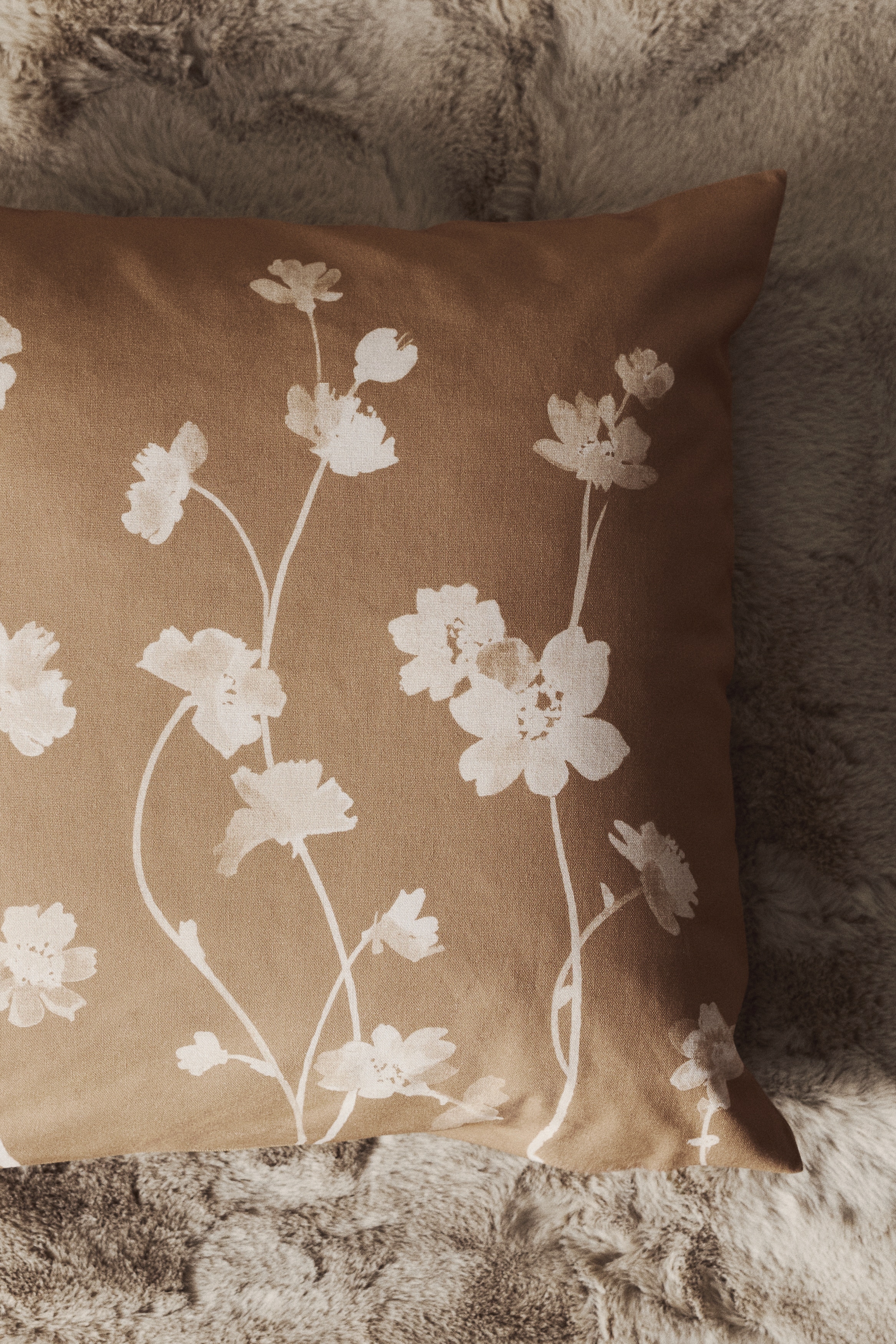 Een kussenhoes is naar voren gericht en toont een botanische print van witte bloemen en stelen op een tan-kleurig katoenen canvas.