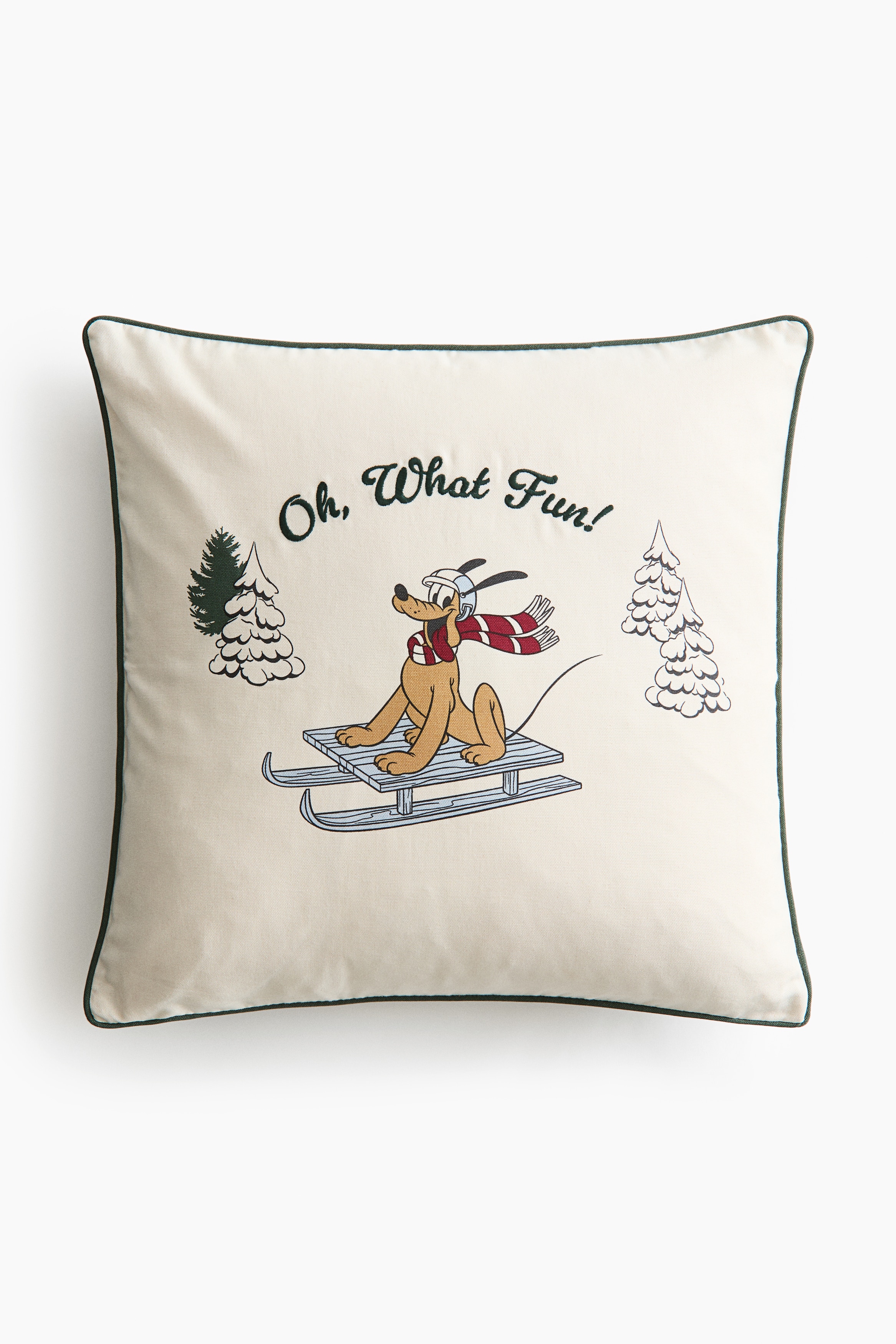 A square off-white cotton canvas cushion cover is shown from the front, featuring a festive printed design of Pluto riding a sled between snow-covered pine trees. The design includes embroidered dark green text reading âOh, What Fun!â arched above the character, with dark green piping detailing the edges.