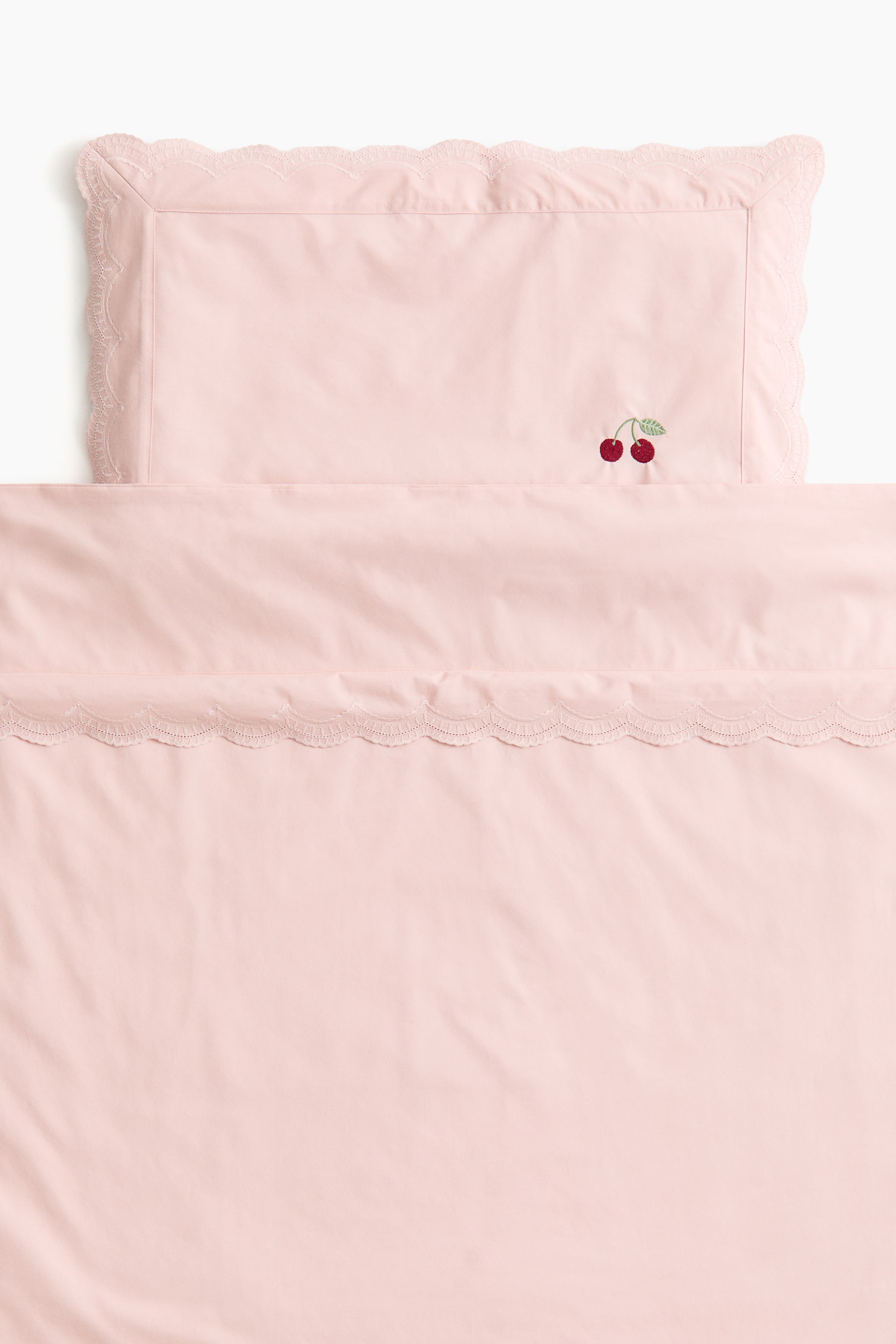 View larger image: The pink pillowcase and matching duvet cover feature scalloped lace trim. The pillowcase displays two embroidered red cherries with green leaves, while the duvet cover showcases coordinating lace along its top edge.