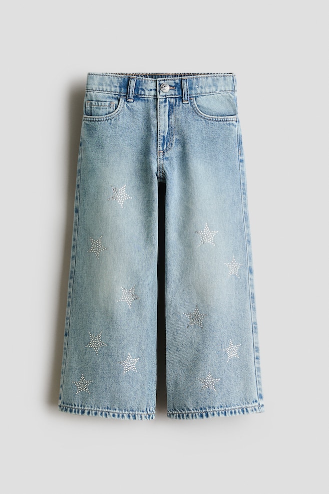 Showing a front view, these light-wash blue denim jeans are featuring a wide-leg, loose fit with a classic five-pocket design and a press-stud closure. The front of both legs is displaying scattered, shimmering rhinestone star embellishments. - 1