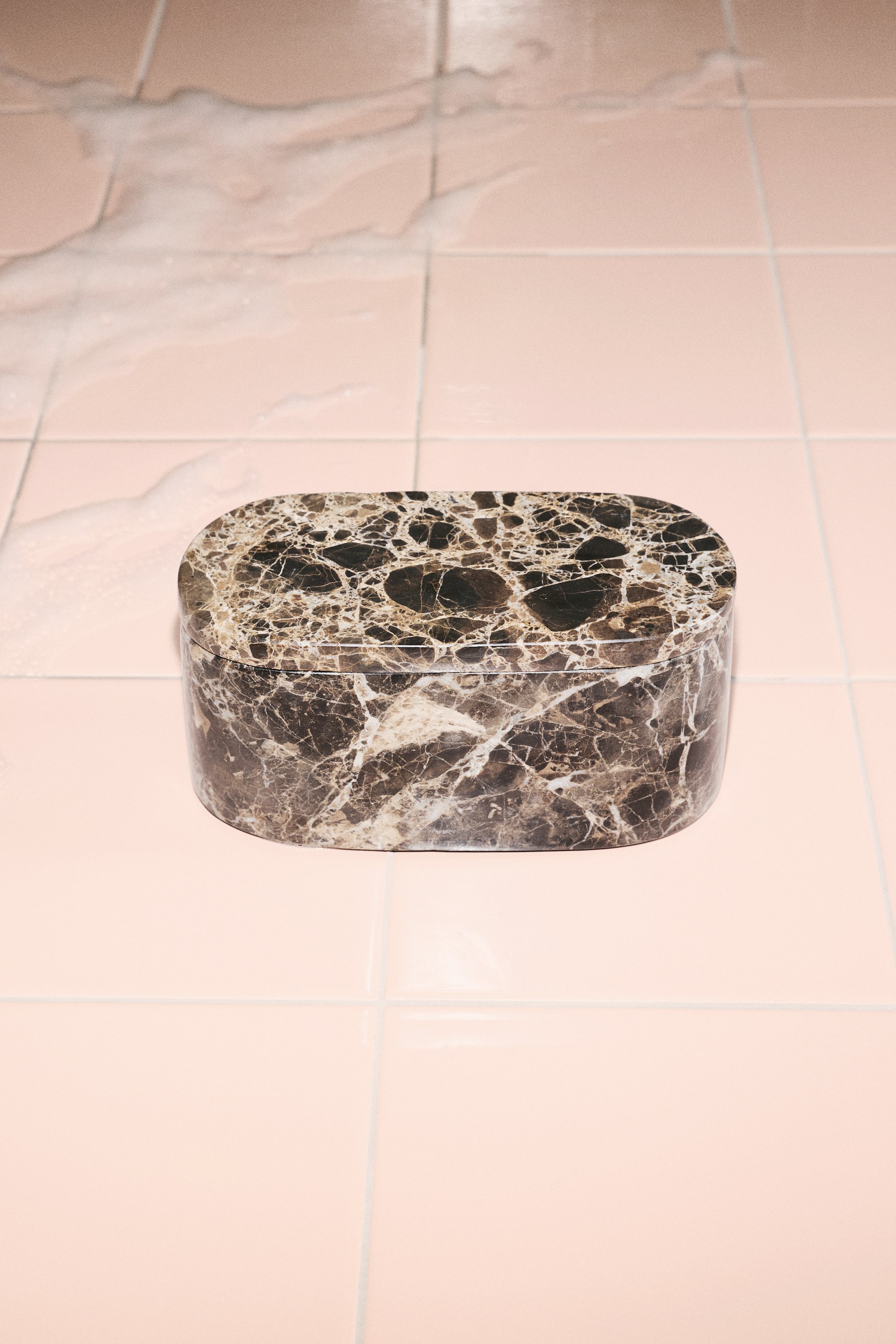 View larger image: An oval lidded box crafted from dark brown marble is shown from a front-facing, slightly elevated angle, highlighting its intricate beige and white veining. The matching flat lid rests securely on the rounded base, showcasing the natural stone’s continuous pattern.