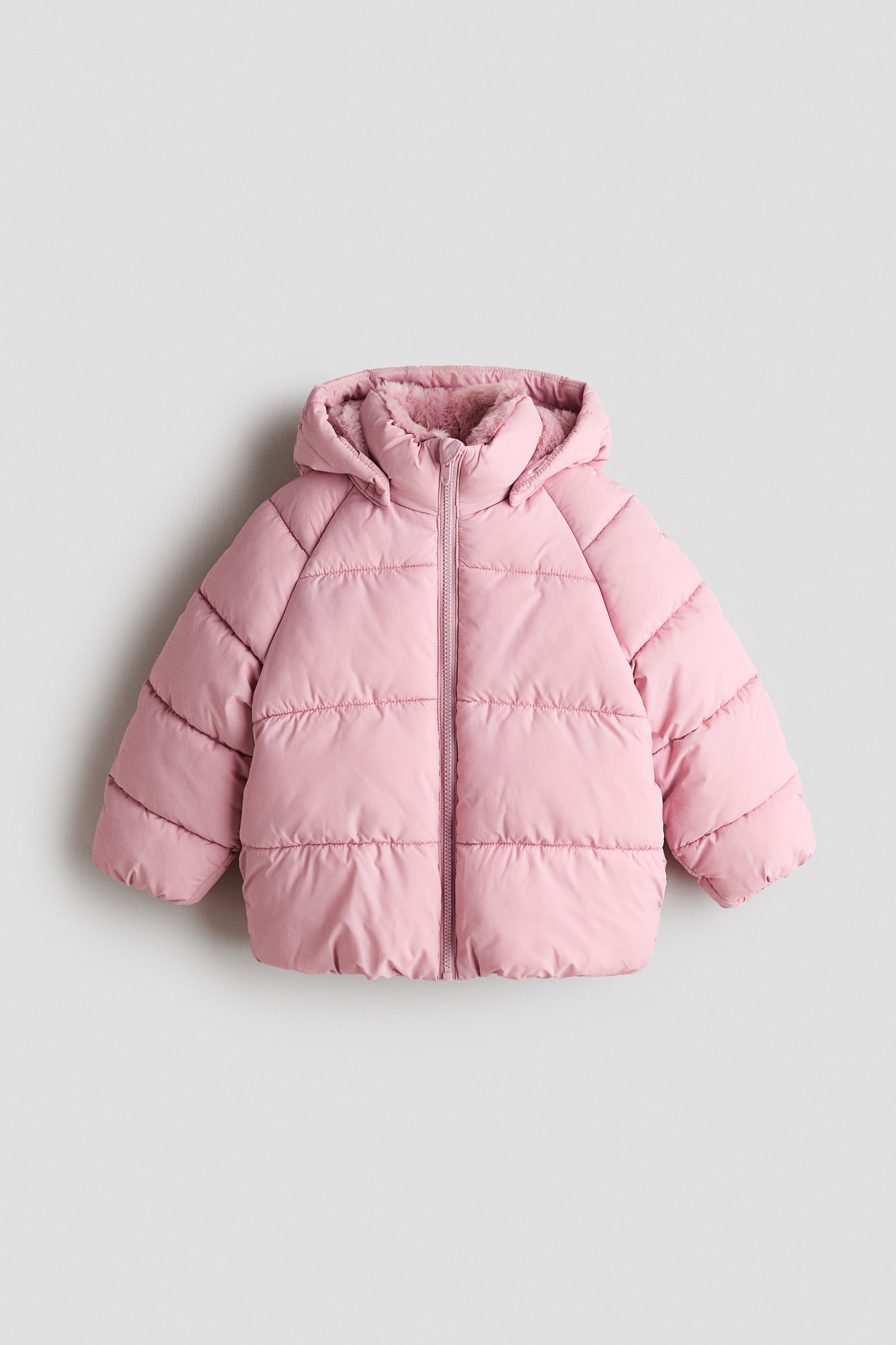 View larger image: A pink puffer jacket is shown from the front, featuring horizontal quilting, raglan sleeves, and a full-length zipper closure. The jacket has an attached hood lined with matching pink faux fur and a high protective collar.