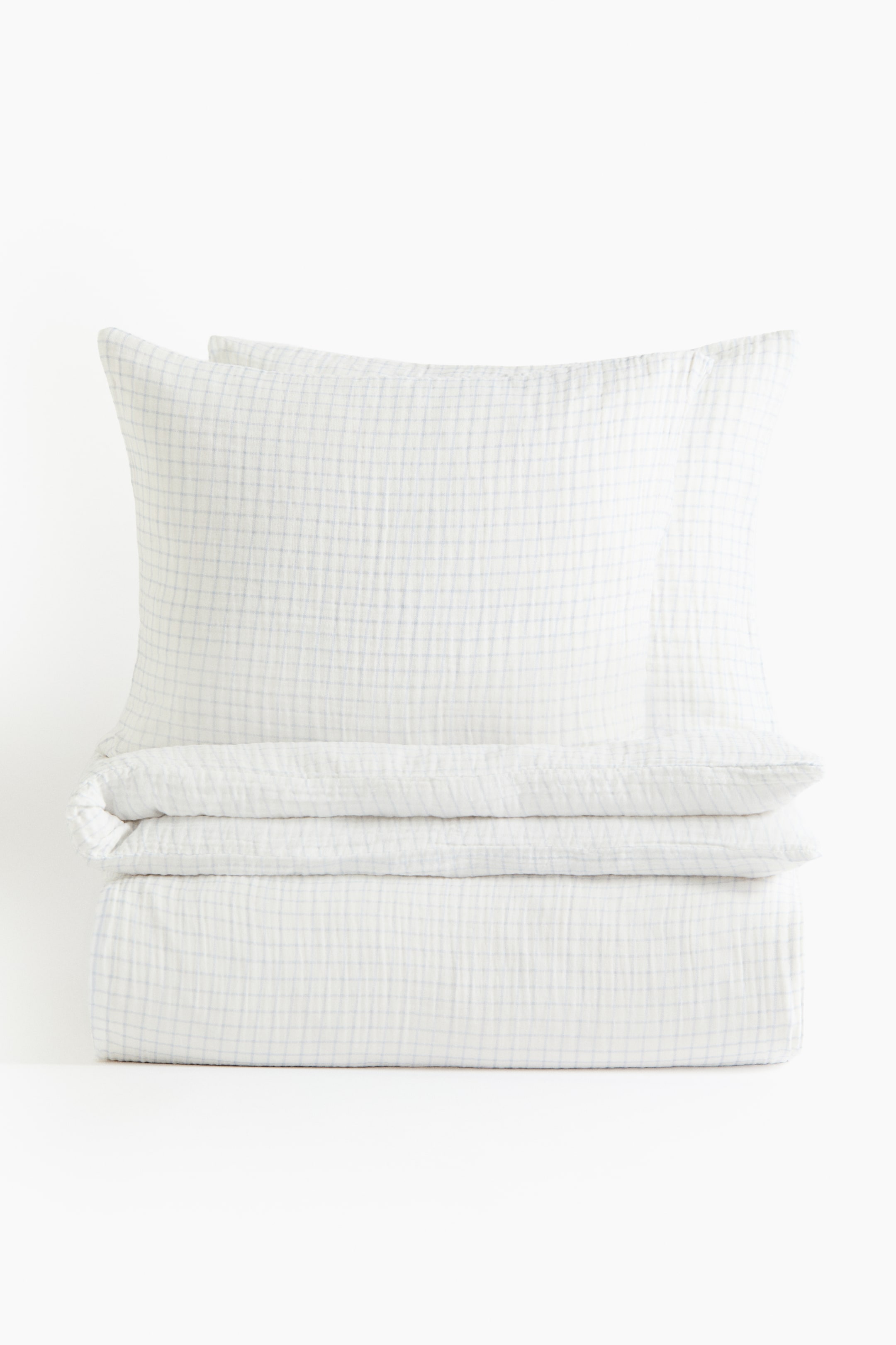 Agrandir l'image: Un ensemble de housse de couette double/king en mousseline est présenté comme un arrangement soigneusement empilé, face avant, avec deux taies d'oreiller reposant sur une housse de couette pliée. Le tissu en mousseline blanche arbore un motif à carreaux bleu clair subtil et une texture froissée.