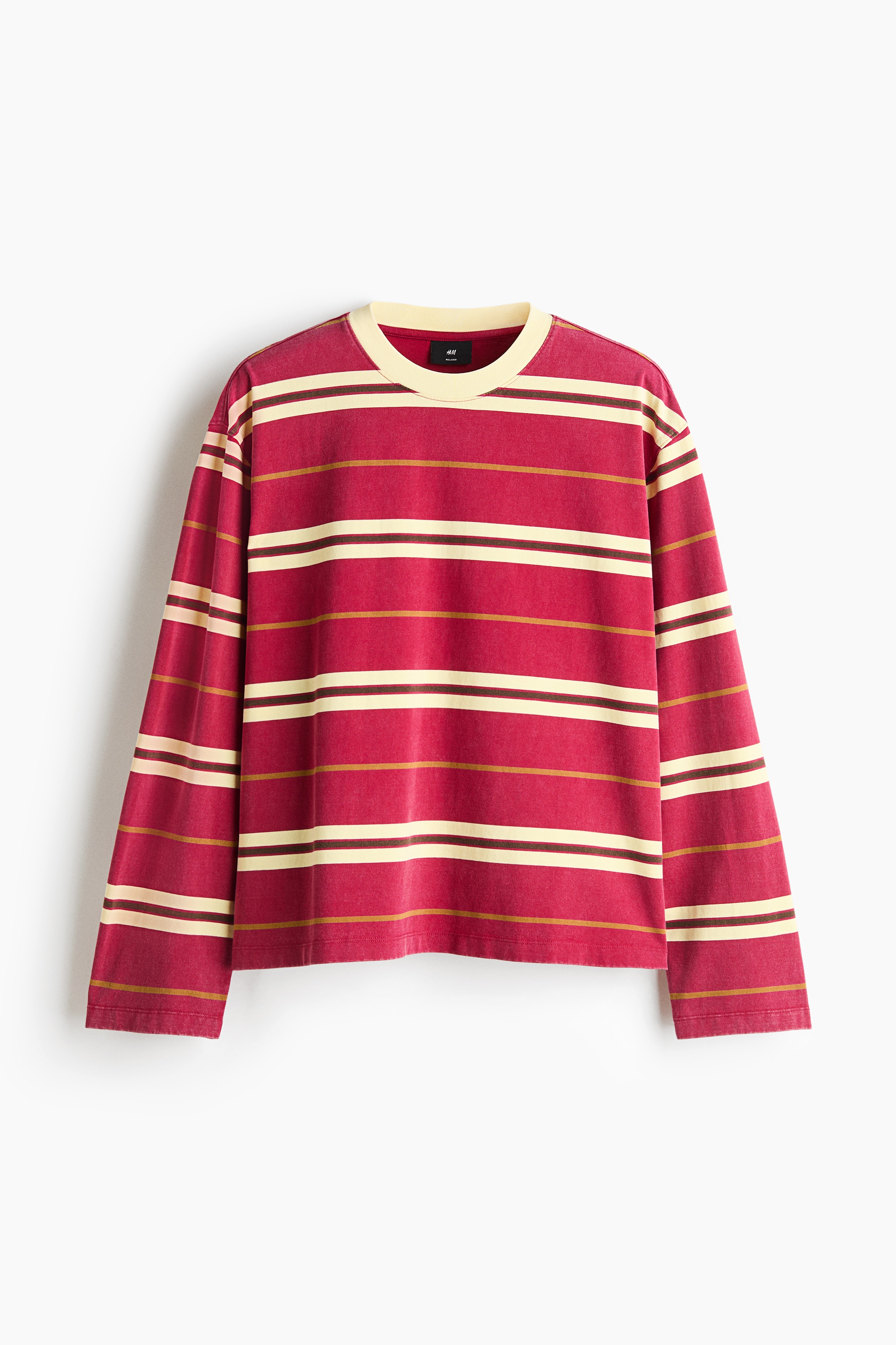 A long-sleeve tee featuring red, cream, and thin brown horizontal stripes is being worn by the model. The relaxed-fit top features dropped shoulders and a cream rib-trimmed neckline, and is styled partially tucked into dark denim jeans.