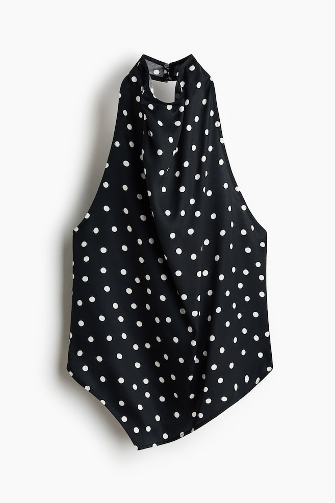 Un haut noir à col halter orné de pois blancs est suspendu pour mettre en valeur son design de face. Il présente un col montant drapé qui se ferme dans le dos, une coupe sans manches et un buste fluide et décontracté avec un ourlet incurvé. - 1