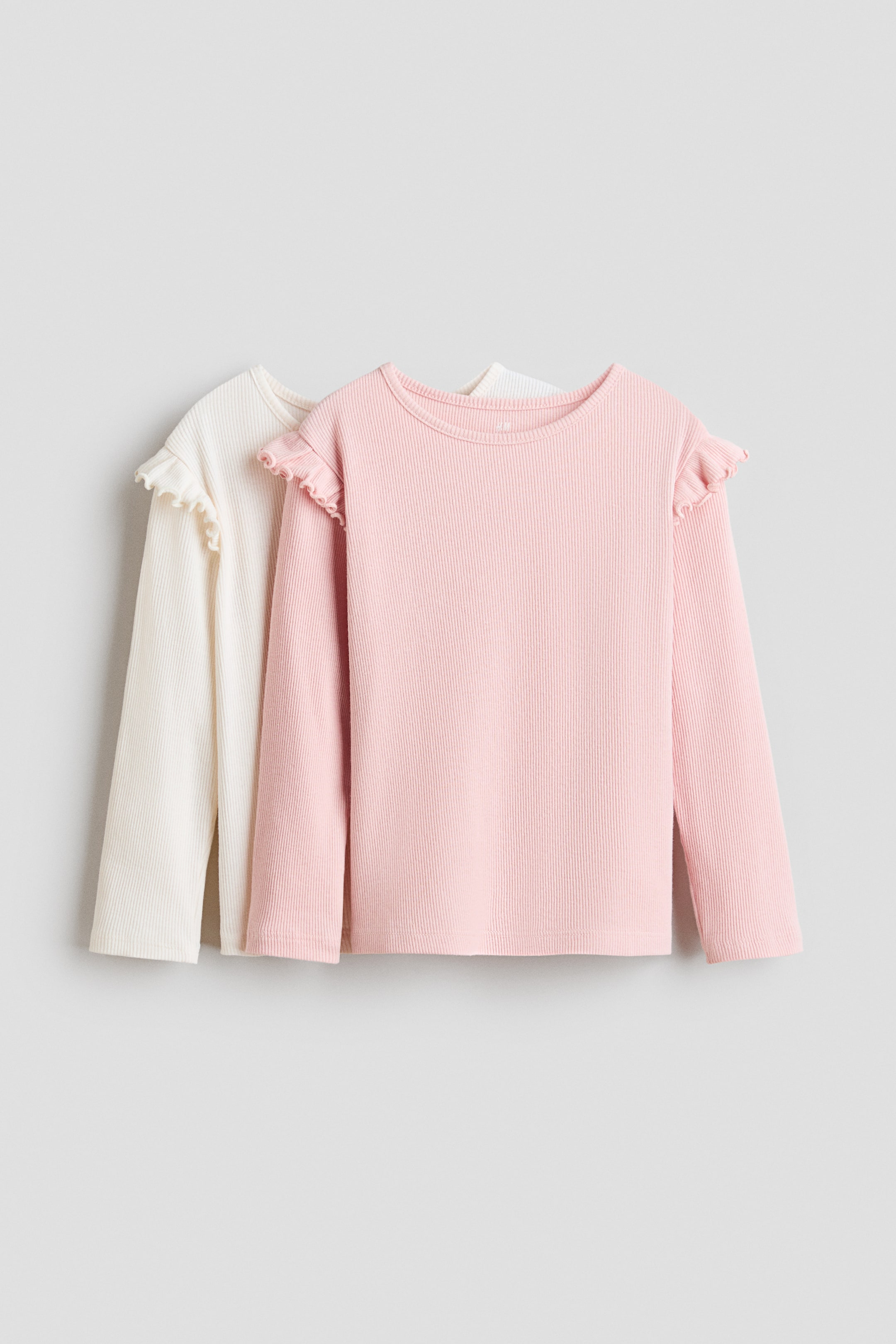 View larger image: Two long-sleeved tops are displayed side-by-side, facing forward. The front top is pink, while the other is off-white. Both garments are crafted from soft, ribbed cotton jersey, featuring a round neckline with a narrow trim and a flounce over the shoulders.