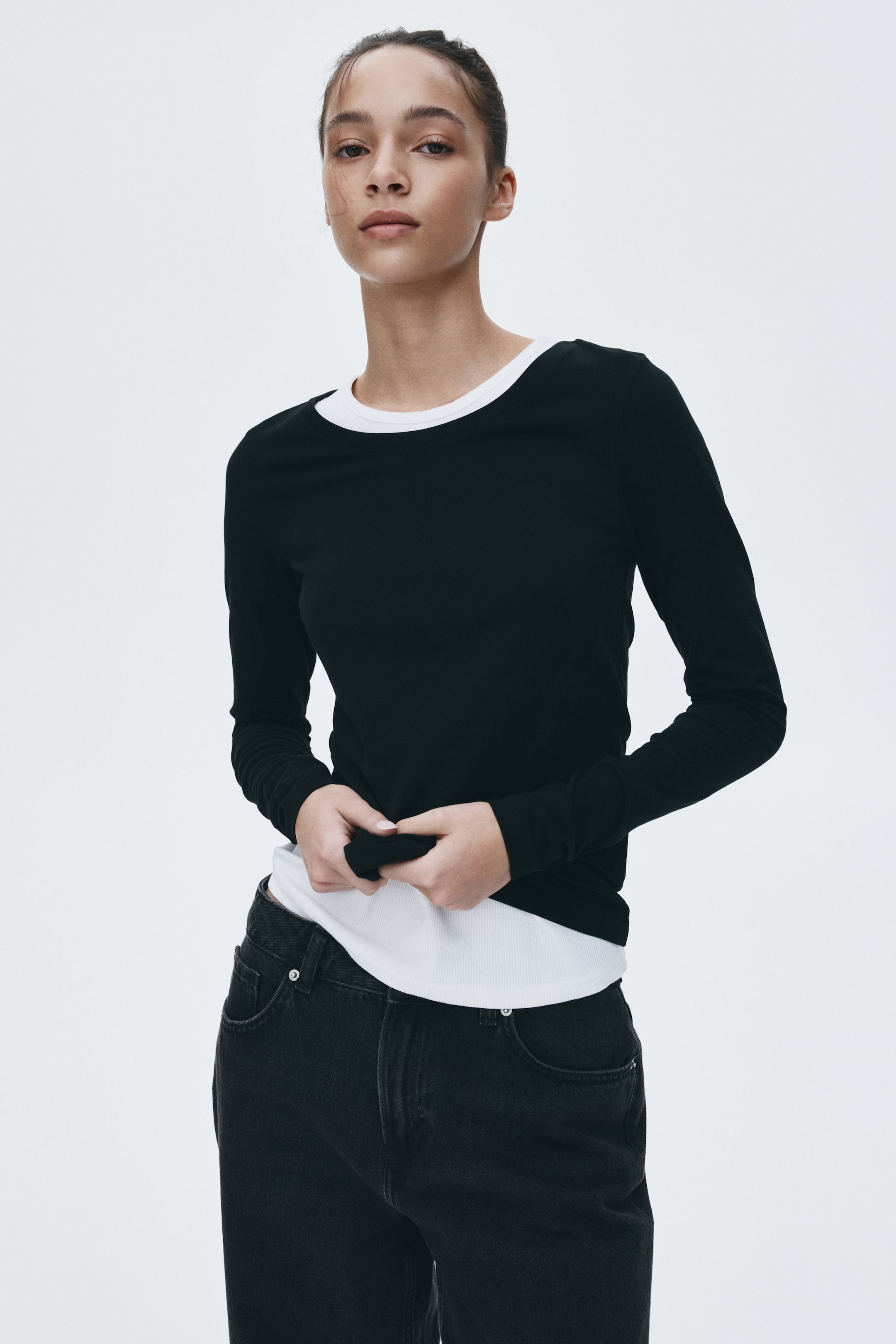 View larger image: A black long-sleeve top, featuring a round neck and smooth fabric, is being worn layered over a white ribbed top, which is visible at the neckline and hem.