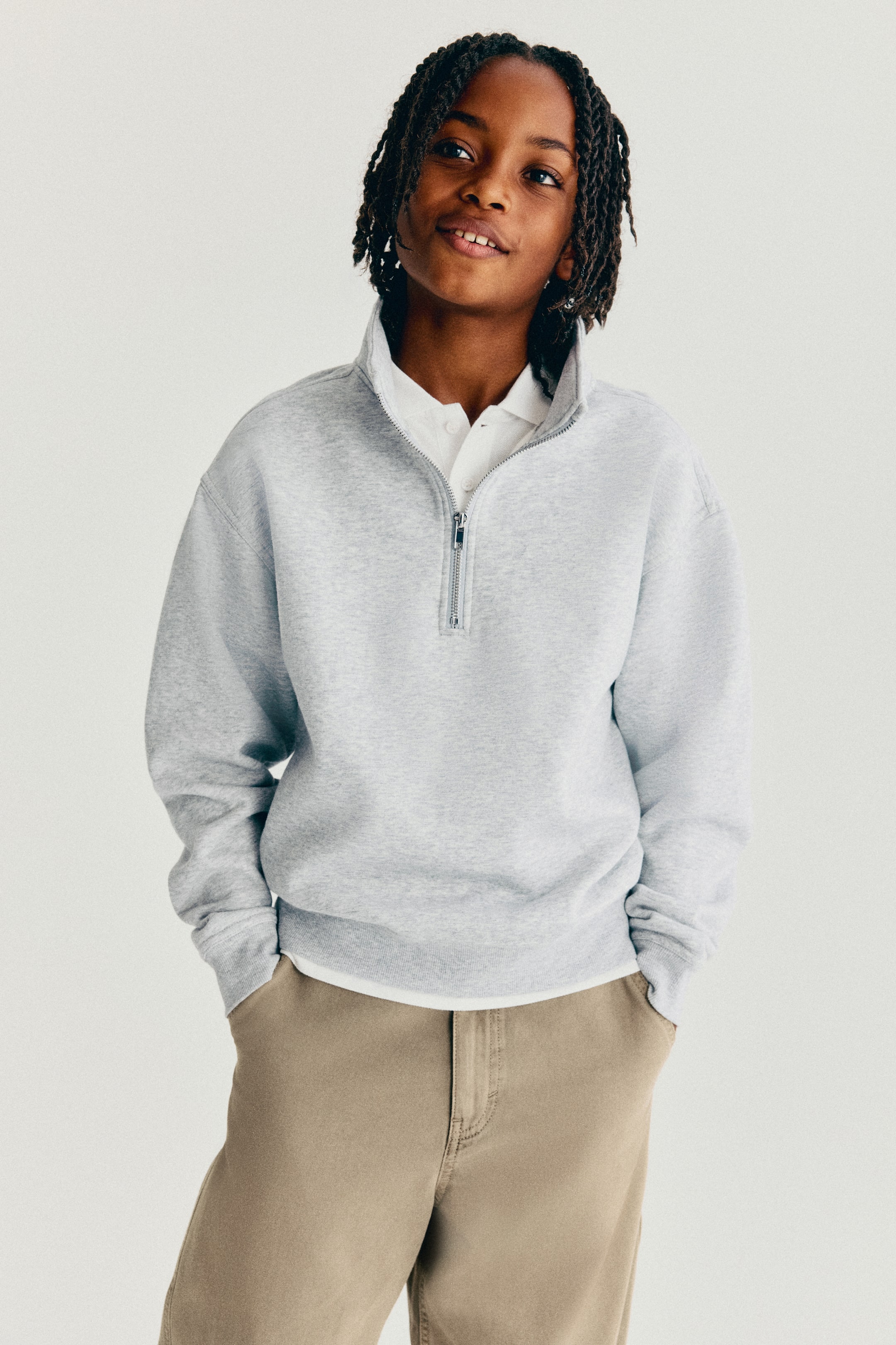 Visa större bild: En ljusgrå sweatshirt i borstad fleece visas framifrån och har en halvlång dragkedja med polokrage, sänkta axlar samt långa ärmar med ribbade muddar och nederkant. Sweatshirten bärs över en vit skjorta med krage för att framhäva dess lediga passform och design.