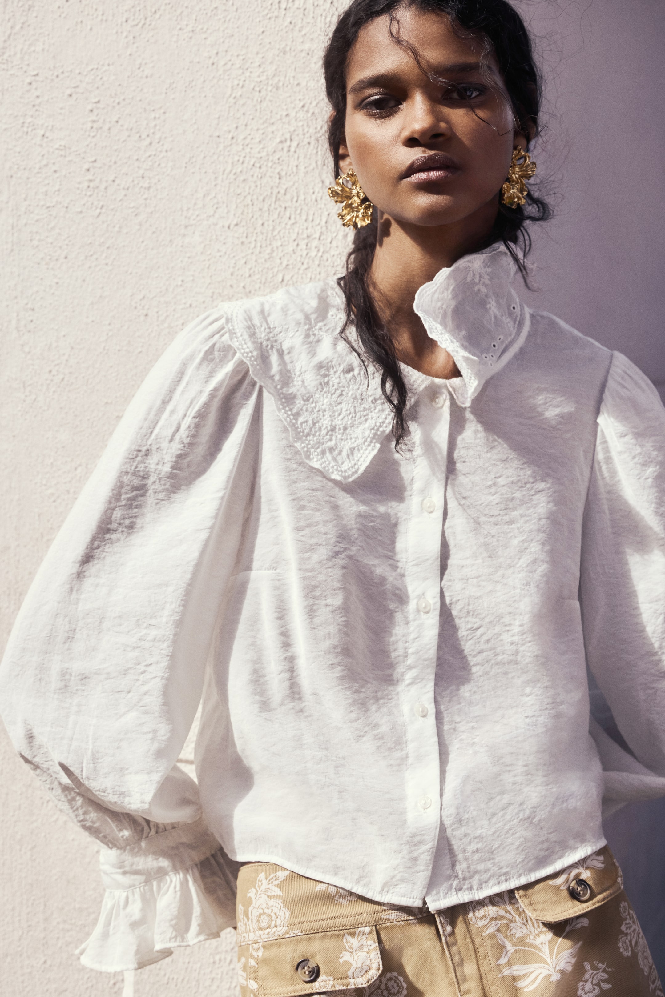View larger image: A white crinkled blouse featuring a large embroidered Peter Pan collar with eyelet detailing. Designed with voluminous puffed sleeves that gather into ruffled cuffs and a button-front placket.