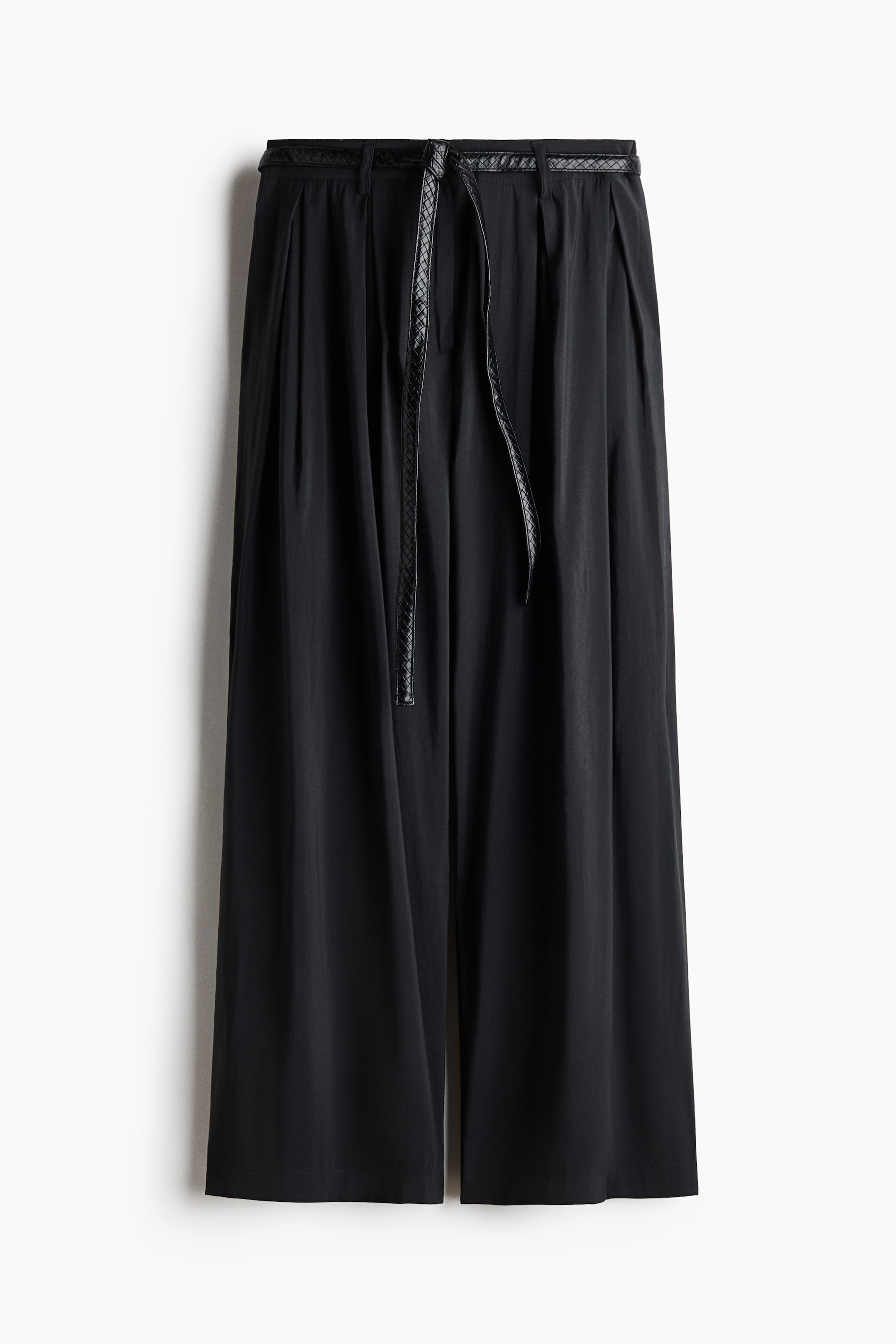 View larger image: Black wide-leg cropped trousers are shown from the front, featuring pleats at the waist. A narrow braided black belt is threaded through the belt loops, with its ends hanging loosely at the front.