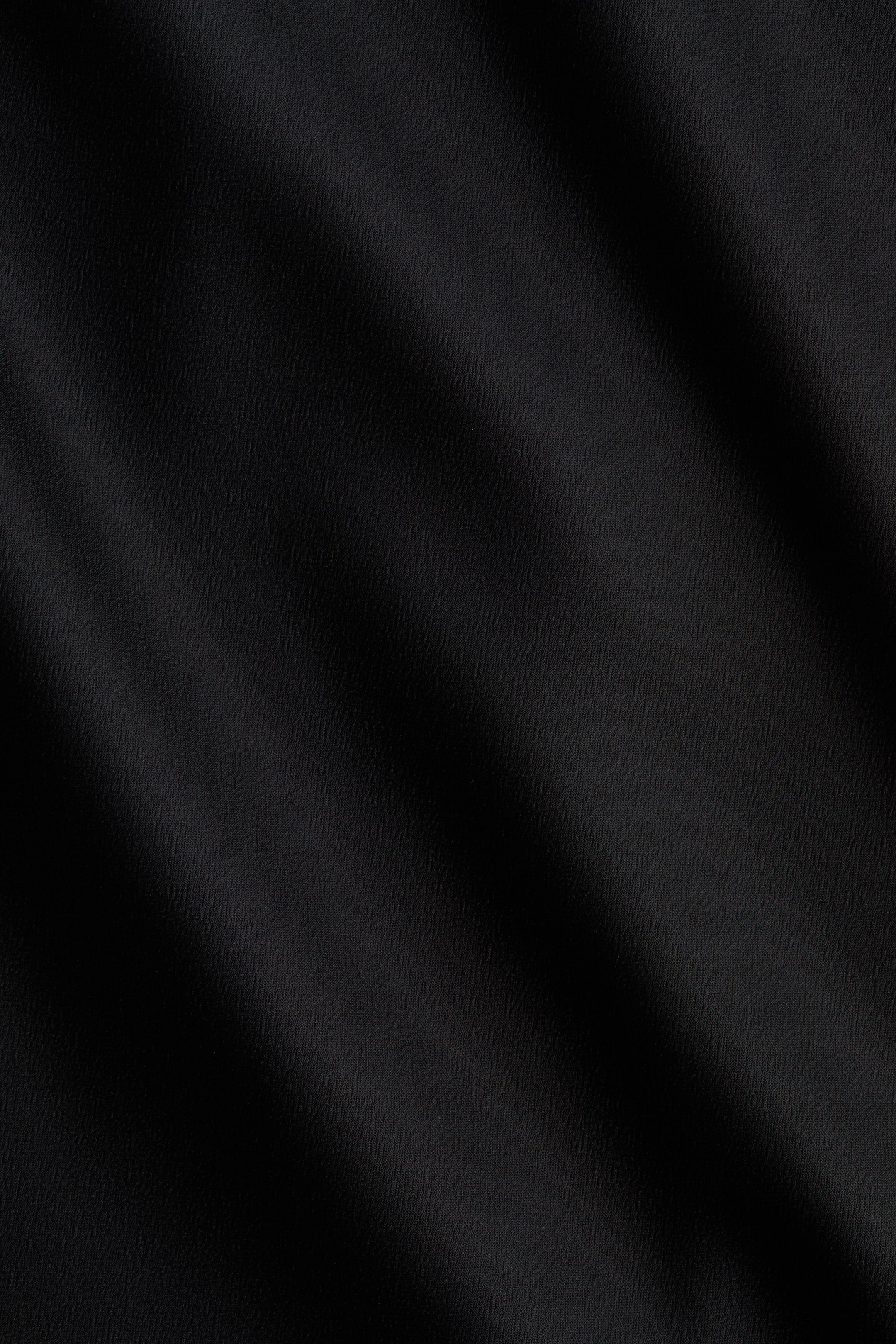 이미지 확대 보기: 발목 길이의 스커트는 부드럽게 드레이프된 검은색 새틴 원단을 선보이며, 부드러운 주름들이 대각선으로 그림자를 만들어 미묘한 질감을 강조하고 있습니다.