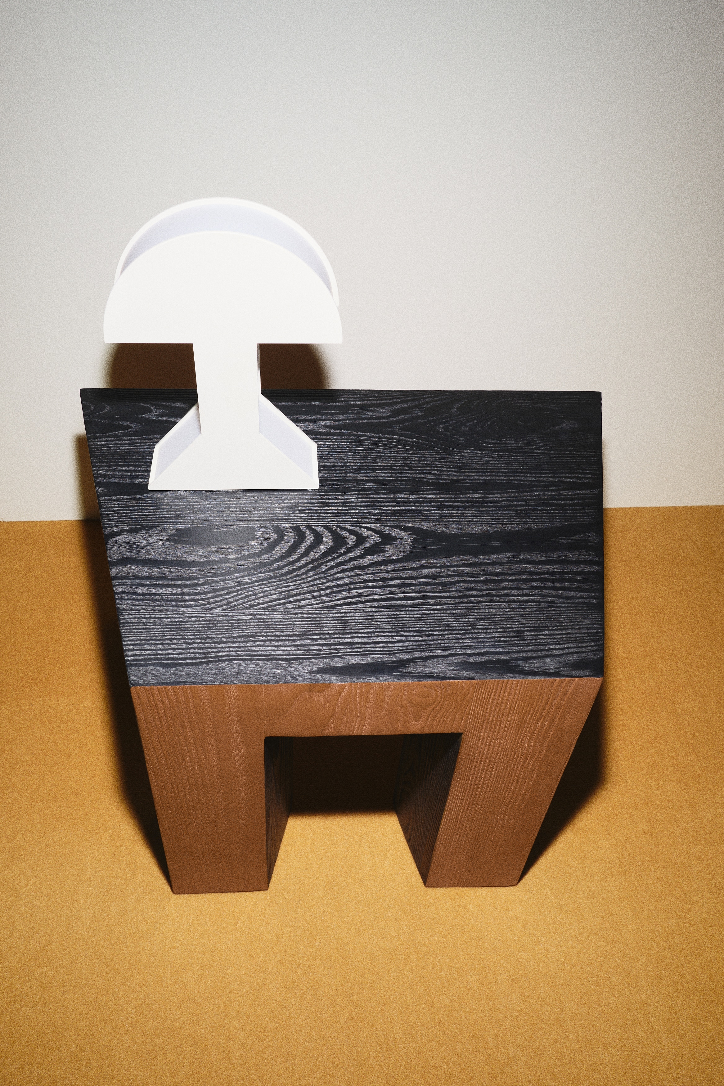 Une lampe de table blanche présente un abat-jour semi-circulaire avec un panneau intérieur visible. Son pied plat blanc est relié à une base trapézoïdale inversée, et un cordon d'alimentation gris clair s'étend à partir de la base.