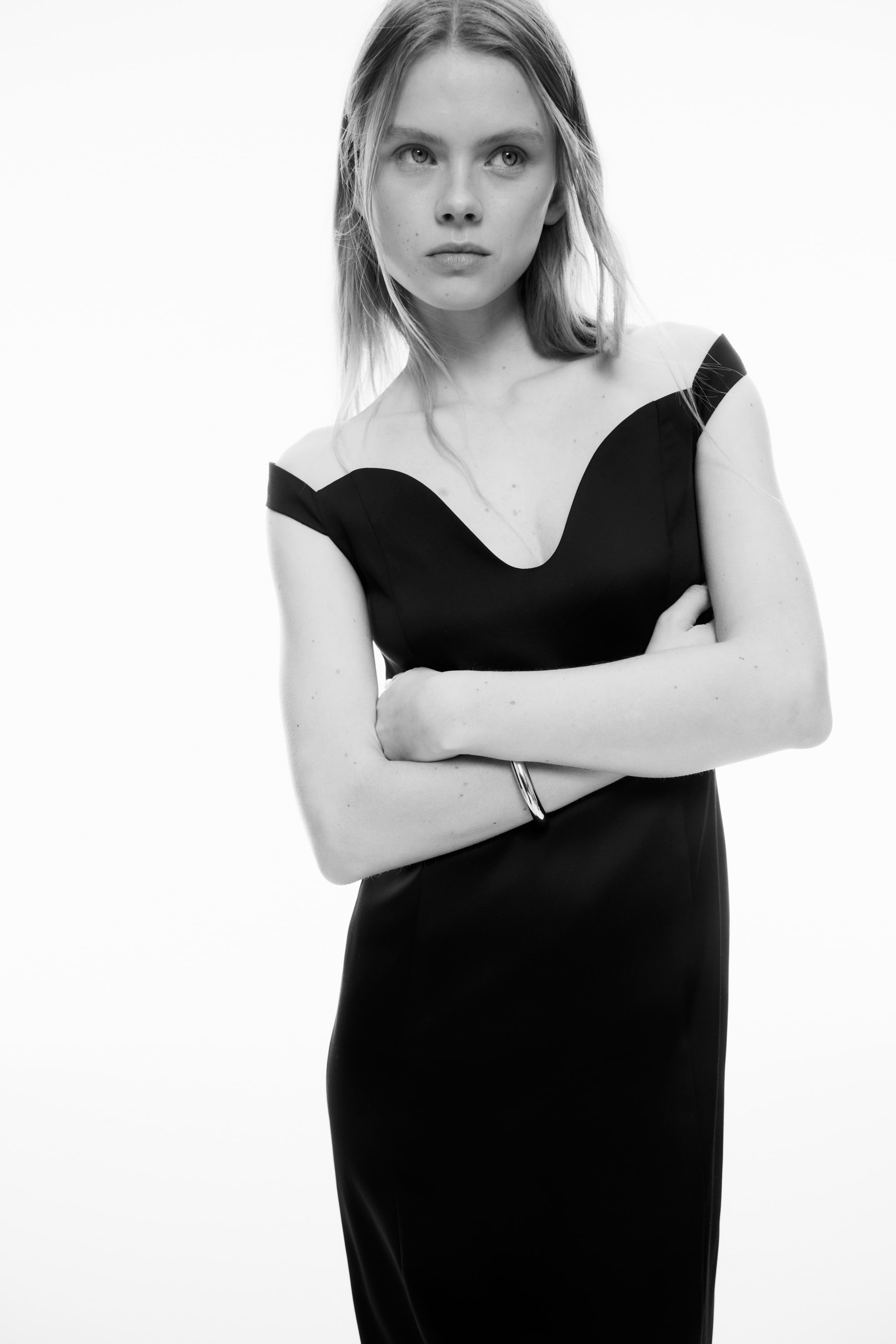 View larger image: A black dress featuring a deep sweetheart neckline with sheer off-the-shoulder panels forming short sleeves. It showcases a fitted silhouette through the bodice.