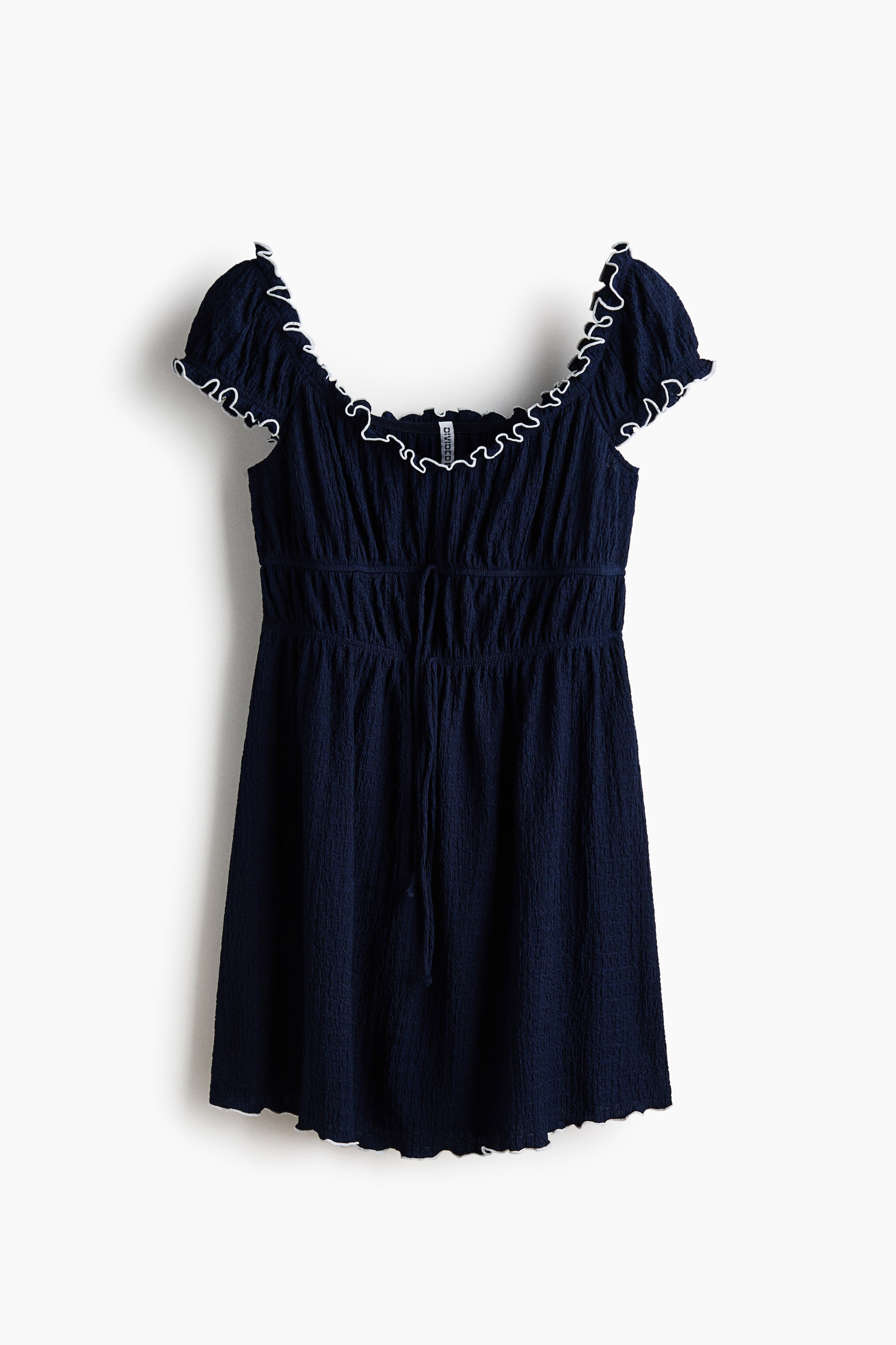 View larger image: A dark blue dress is shown facing front, featuring a crinkled texture throughout, a wide ruffled neckline and short puffed sleeves, all edged with white trim. A matching drawstring cinches the elasticised waist, and the dress finishes with a wavy hemline also detailed with white ruffles.