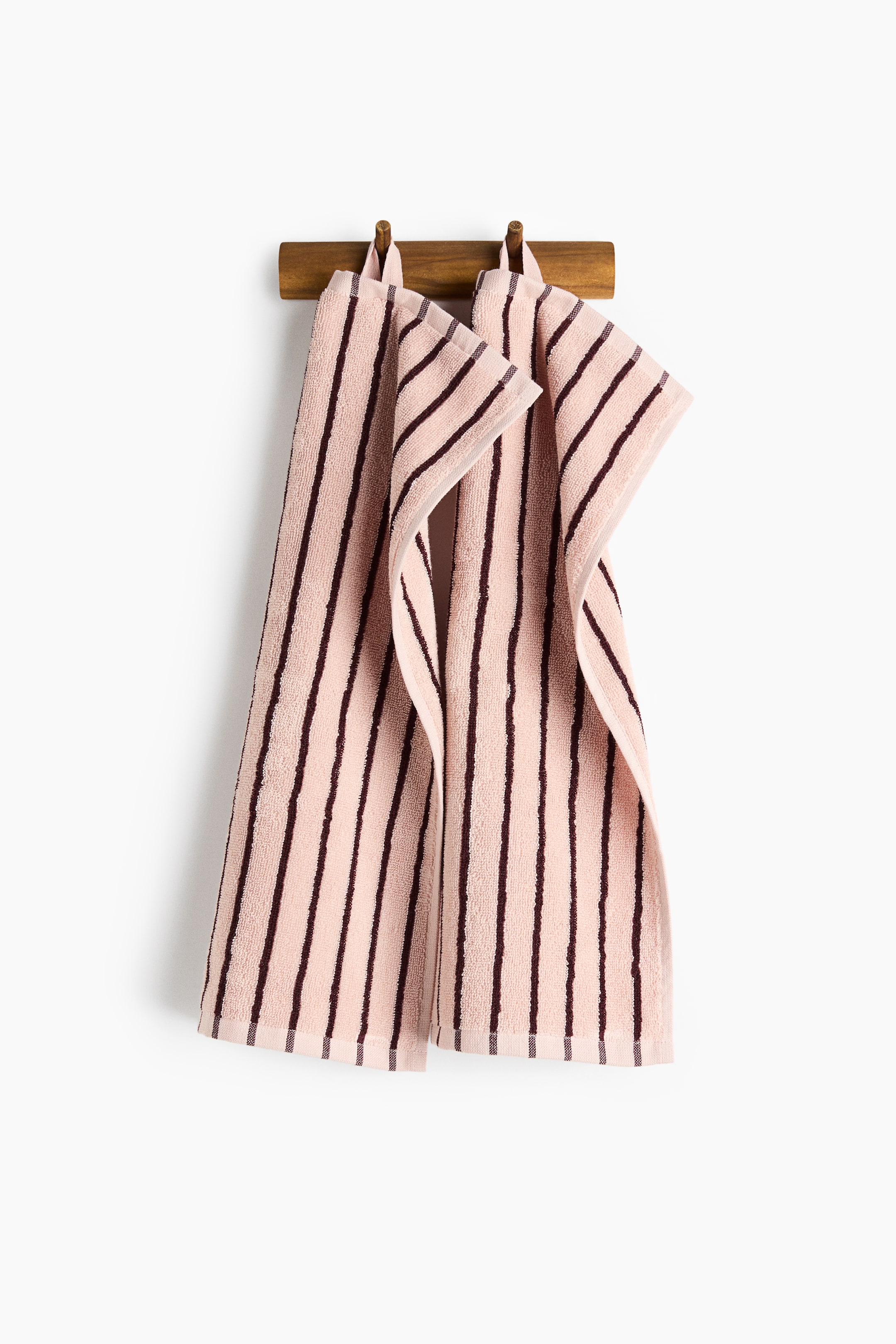 View larger image: A pair of guest towels is hanging by loops, facing front, showcasing a timeless striped pattern in blush pink and dark brown on soft cotton terry. Each towel is adorned with a woven hem.