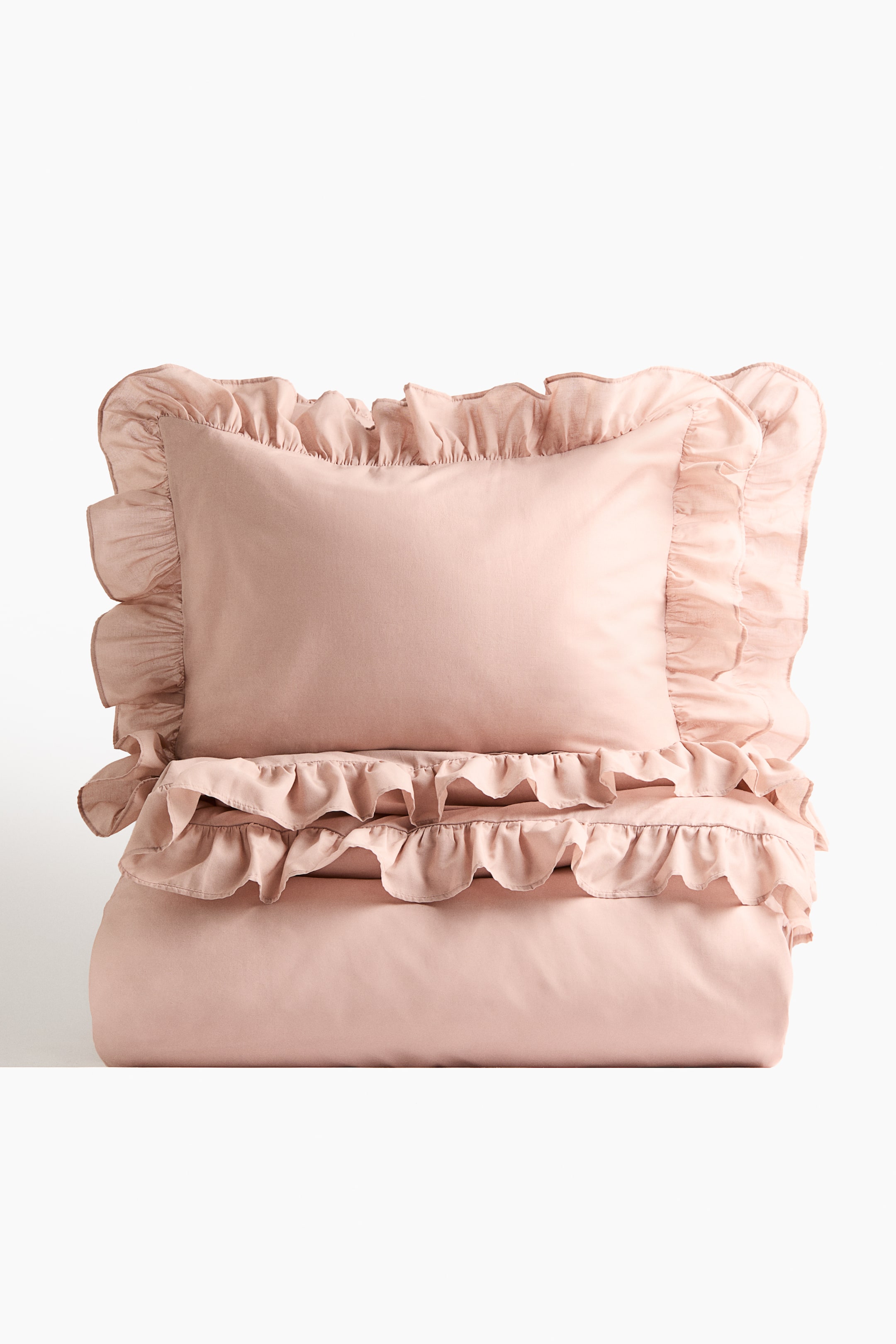 View larger image: A light pink duvet cover set is presented, with one pillowcase lying flat, facing forwards, on top of a neatly folded duvet cover. Both the pillowcase and the top edge of the duvet cover display lavish flounces.