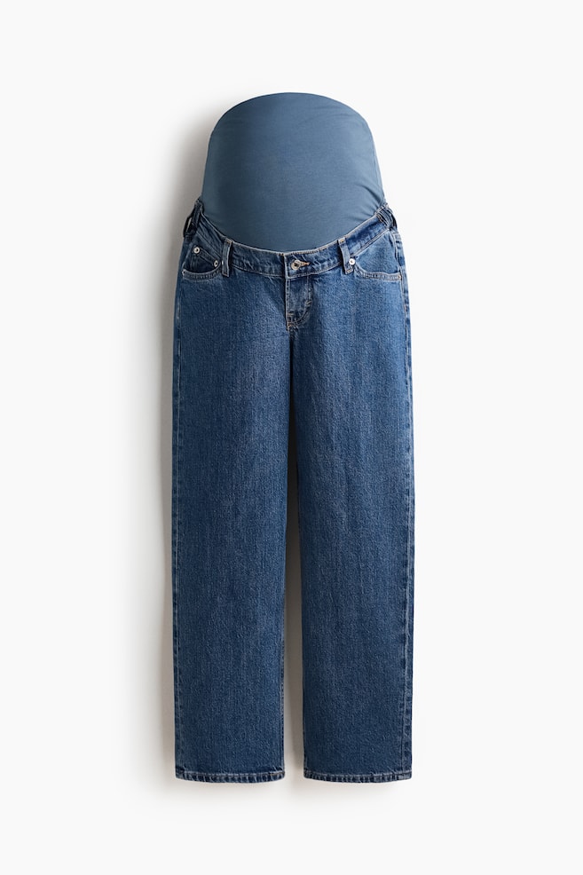 Een paar blauwe 5-pocket denim zwangerschapsjeans met een rechte pijp en een reguliere pasvorm van de taille tot de heup, die losser valt van de dij tot de enkel-lange zoom. Een brede blauwe jerseyband bedekt de taille, en een nep gulp met een knoop is zichtbaar aan de voorkant. - 1