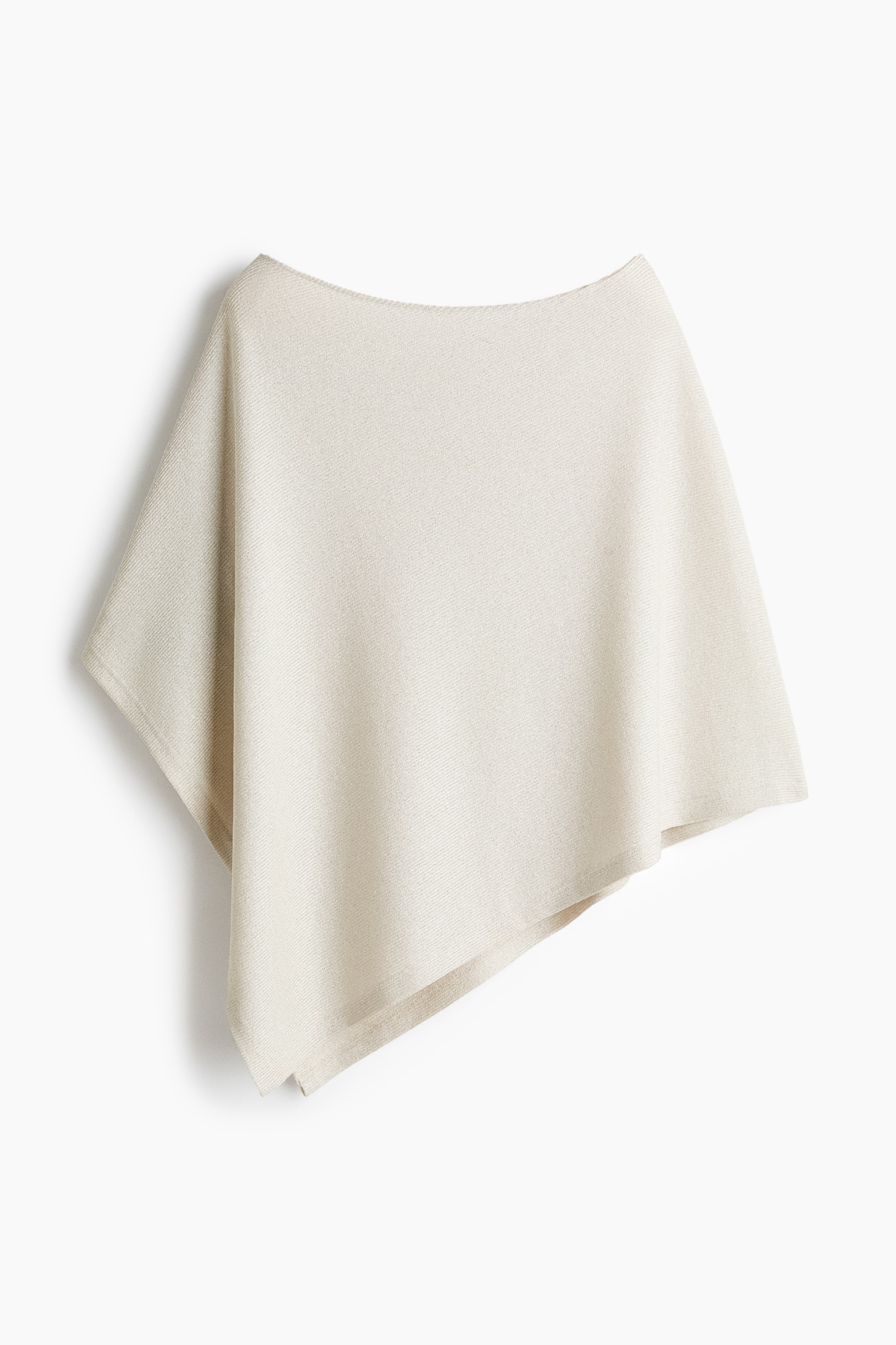 View larger image: A knit poncho in a light cream hue is hanging from a front angle, showcasing a wide boat neckline and a fine-textured weave. The garment is draping loosely to create an asymmetrical, angular hemline.