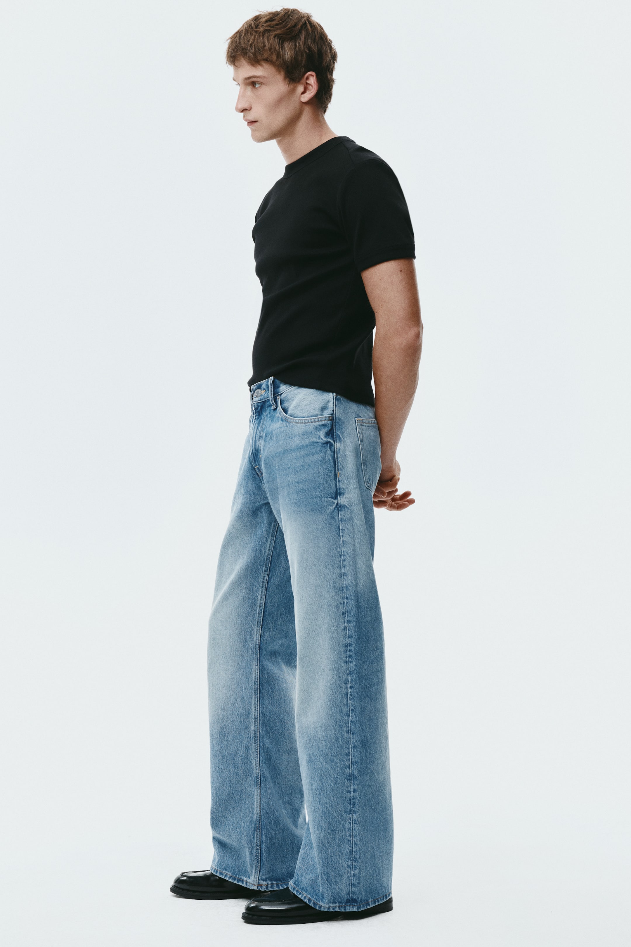 View larger image: Light-blue wide-leg jeans are shown in a relaxed fit from a slight side-front angle. The jeans feature a light wash with subtle fading and pool over the wearer’s shoes, showcasing their full length.
