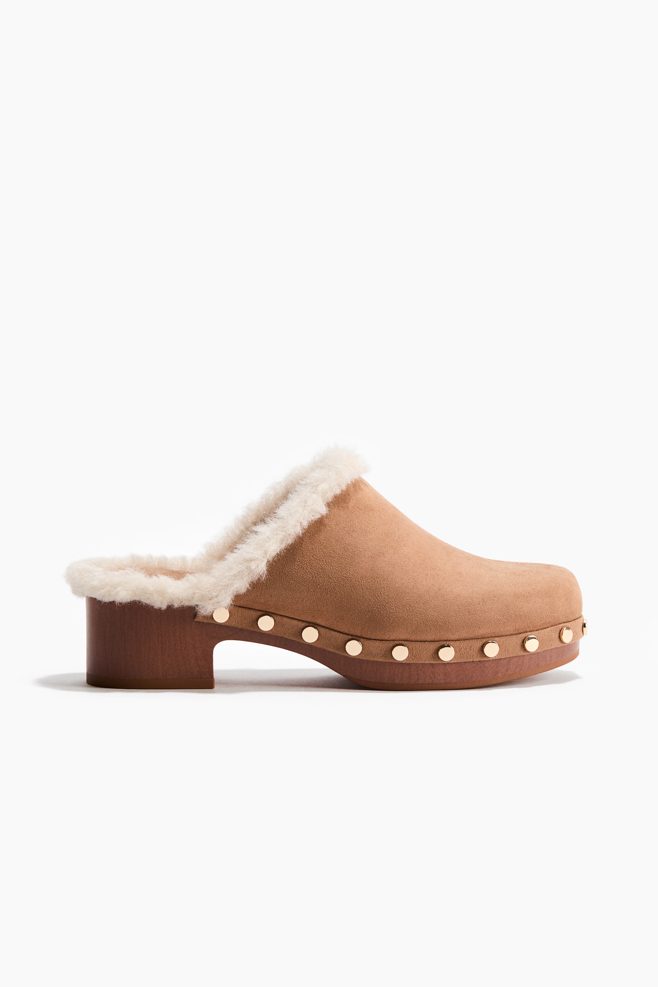 View larger image: A tan suede clog featuring a cream faux shearling lining visible along the opening. Gold-tone studs detail the wooden-look platform sole and block heel.