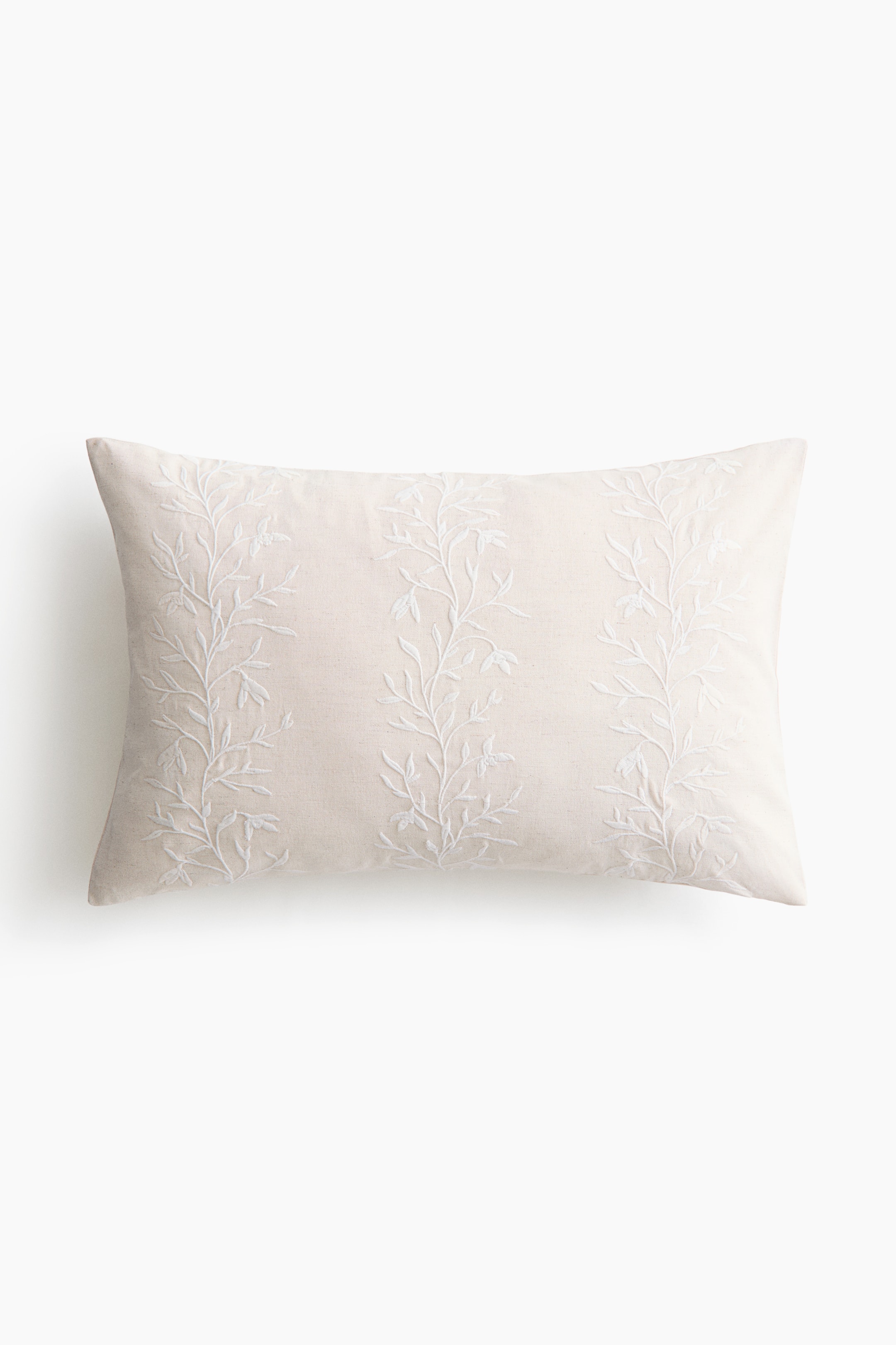 View larger image: A rectangular lumbar pillow in a light beige fabric is facing front, showcasing three vertical columns of delicate white embroidered vine and leaf motifs. The textured woven fabric presents a clean-lined, structured appearance with neatly stitched edges.