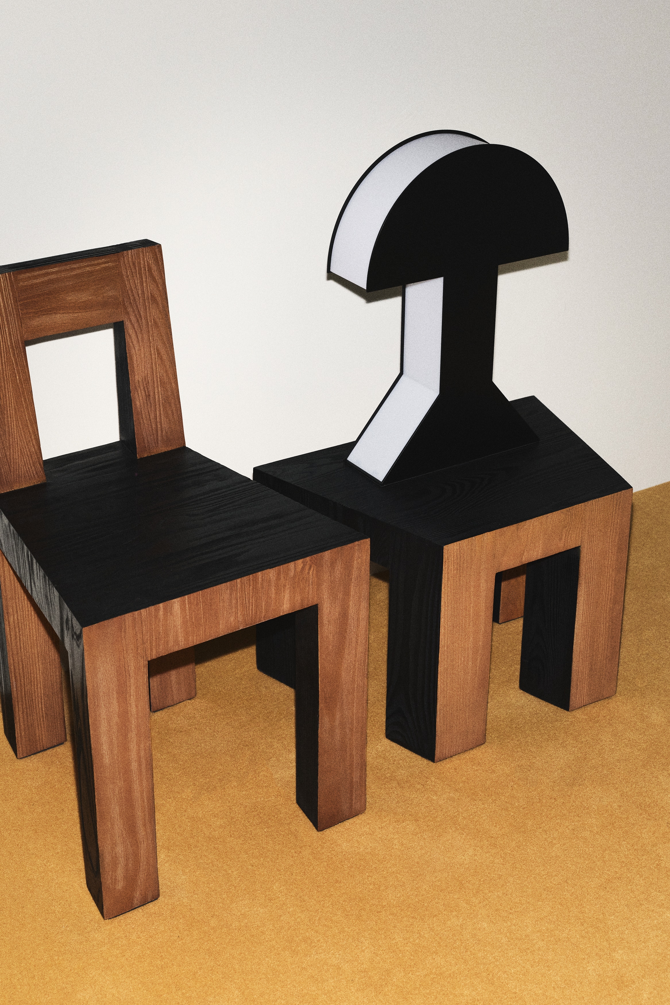 Une lampe géométrique noire présente un sommet semi-circulaire, une tige rectangulaire et une base trapézoïdale. Une lumière blanche illumine les bords intérieurs du sommet, de la tige et de la base. Un cordon d'alimentation noir s'étend depuis le coin inférieur gauche de la base.