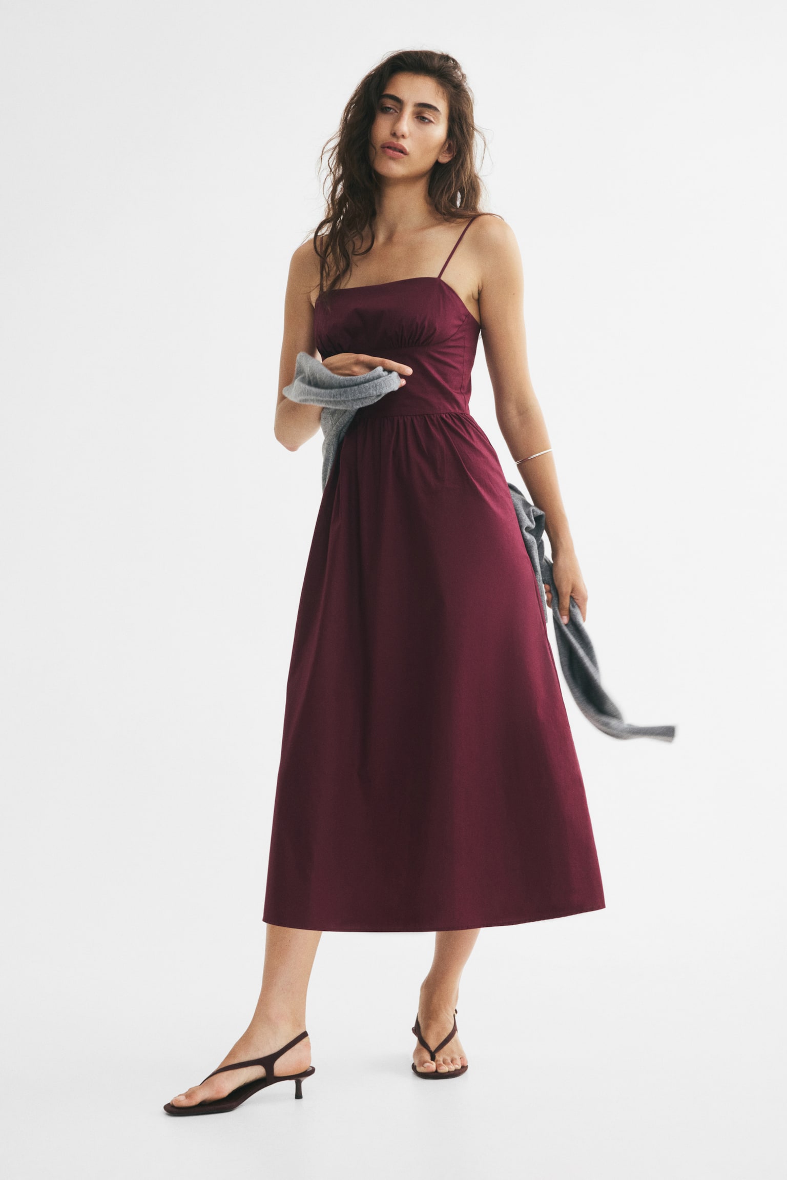 A burgundy midi dress is featuring a straight neckline with thin spaghetti straps, and a fitted bodice displaying horizontal ruching across the bust. The gathered waistline is leading to an A-line skirt. - 1