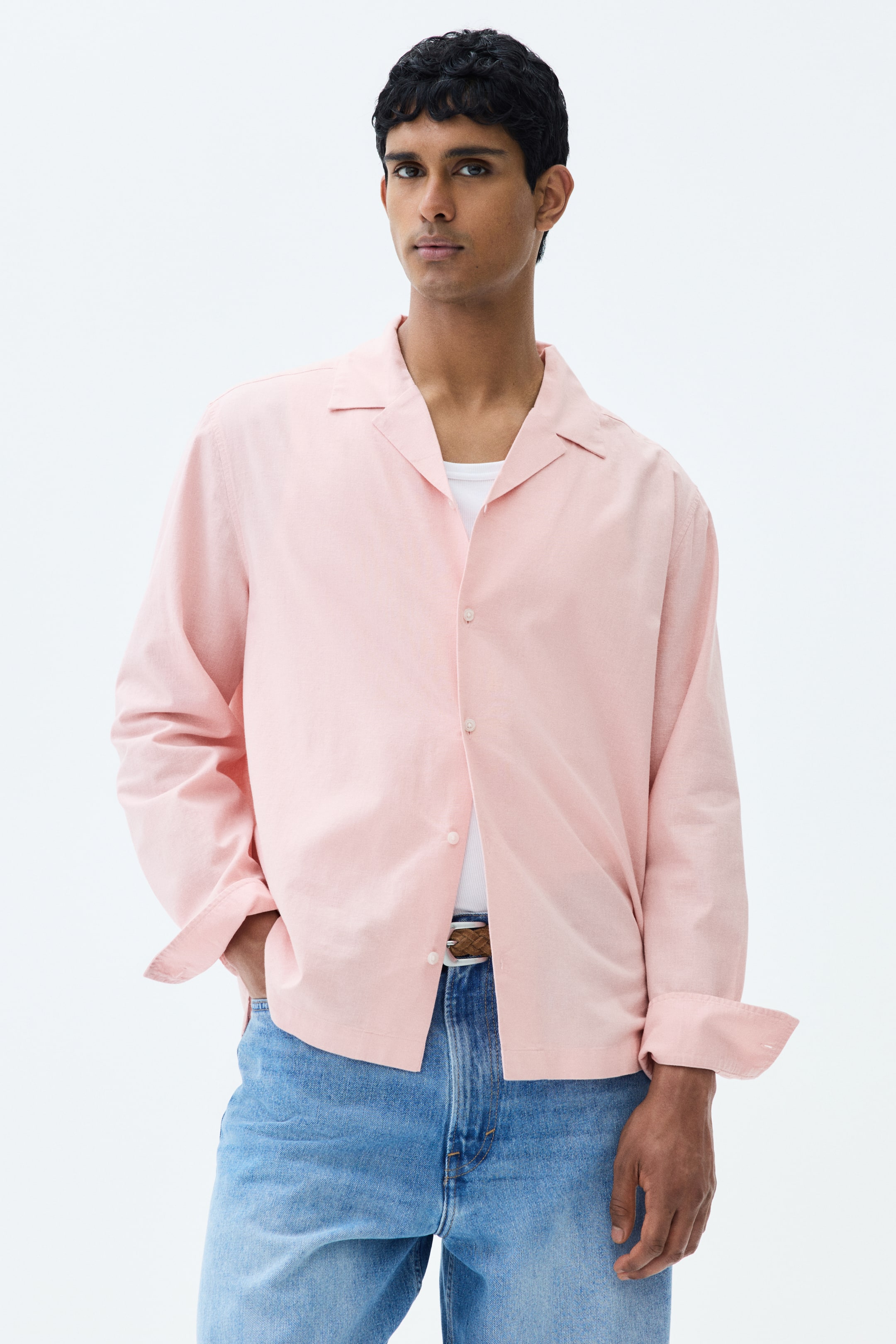 View larger image: A pink long-sleeved shirt with a resort collar and French front is worn open over a white undershirt. The shirt features rolled-up cuffs and a straight hem, with the model posing with one hand in a pocket, highlighting its relaxed fit.