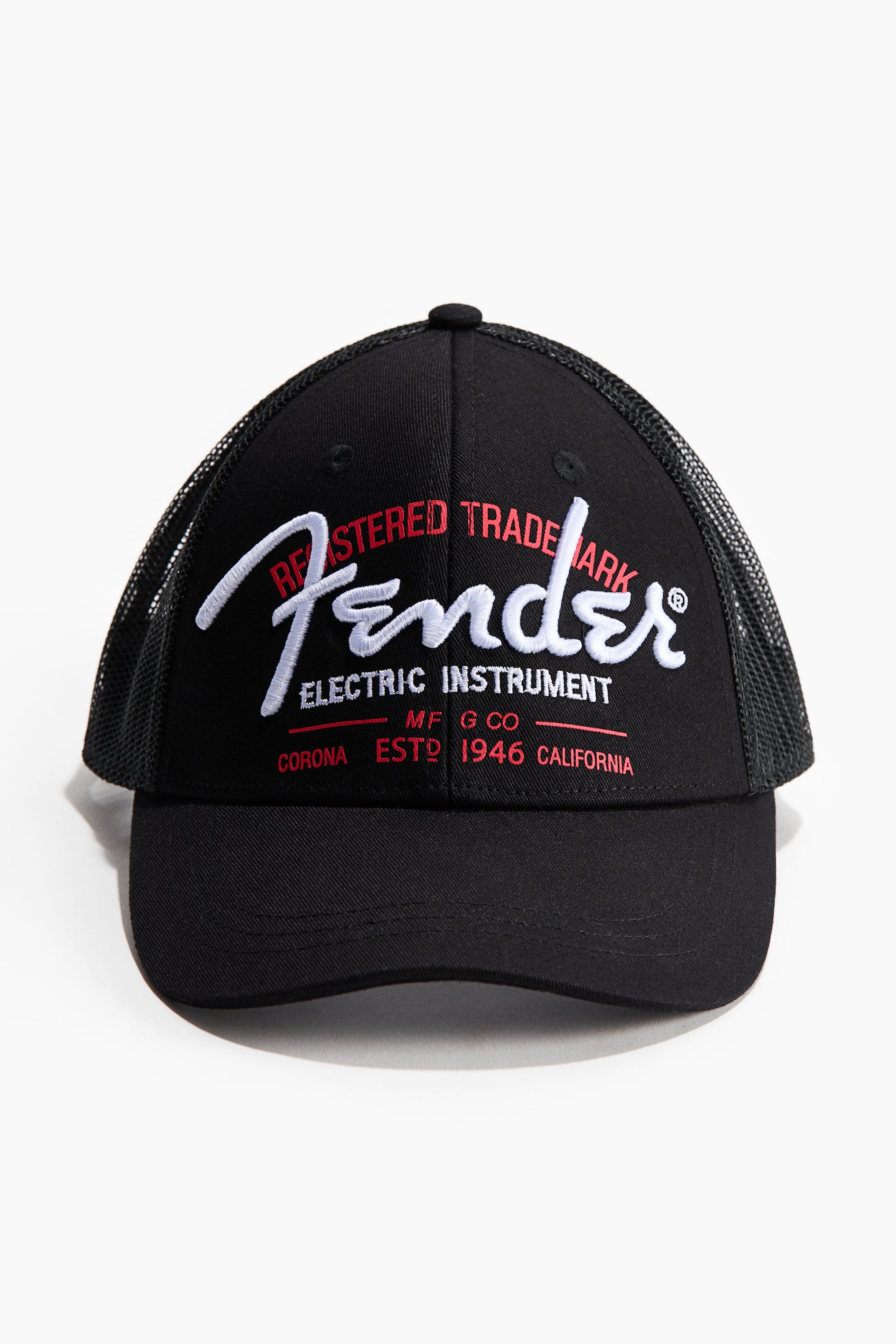Grotere afbeelding bekijken: Een zwarte truckerpet is naar VOREN gericht, met een gestructureerd voorpaneel en een mesh achterkant. Op de voorkant staat wit geborduurde 'Fender' letters, vergezeld van rode geborduurde tekst waaronder 'REGISTERED TRADEMARK' en 'ELECTRIC INSTRUMENT MFG CO CORONA ESTD 1946 CALIFORNIA'.